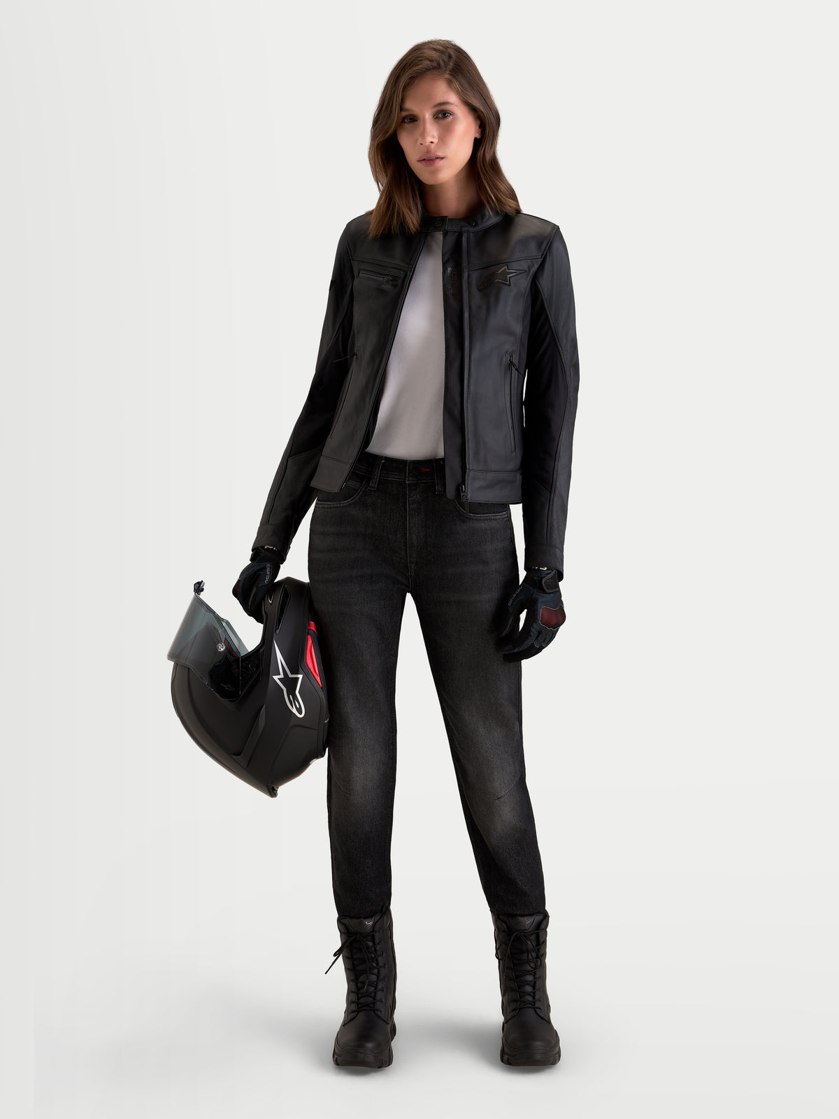 Alpinestars Stella Flex-AST 5 Denim, calças de ganga de moto urbanas para mulher, preto lavado, com proteção CE, usadas por um modelo a segurar um capacete e a vestir casaco e botas de moto a combinar