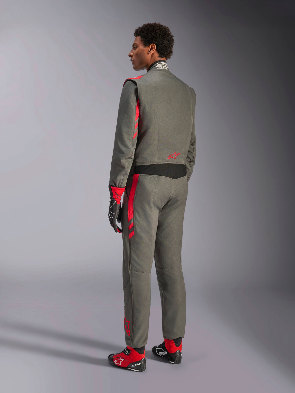 Alpinestars GP Race V3 Suit FIA, fato de corrida em Antracite Vermelho, vista traseira de modelo a usar o fato de duas camadas, detalhes vermelhos nos ombros e pernas, combinado com luvas e botas a condizer, equipamento profissional de automobilismo