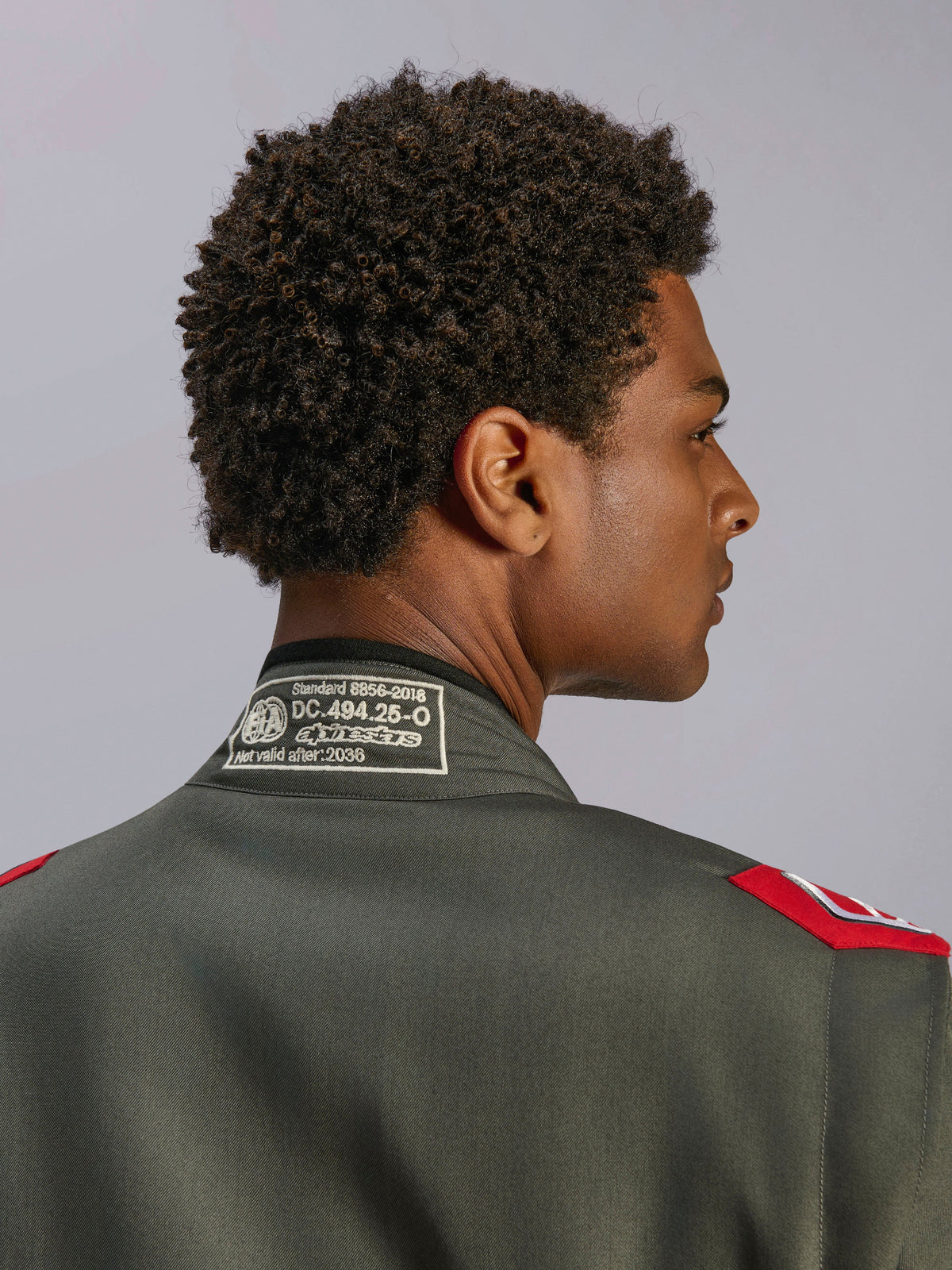 Alpinestars GP Race V3 Suit FIA, fato de corrida em antracite e vermelho, grande plano da parte de trás da gola com etiqueta de certificação FIA 8856-2018 e dragonas vermelhas nos ombros, detalhe de vestuário de automobilismo profissional