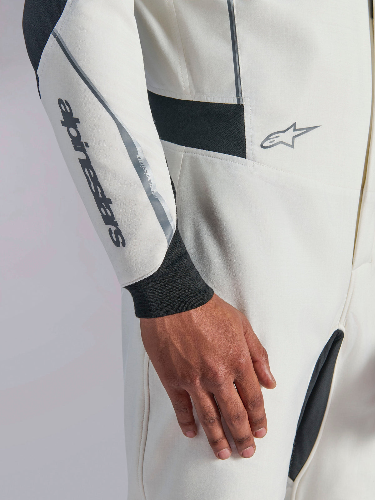 Fato Alpinestars Hypertech V3, grande plano de fato de automobilismo branco com detalhes em preto e prateado, logótipo Alpinestars no antebraço, punho de malha preto e painéis elásticos escuros para mobilidade, vestuário profissional de automobilismo