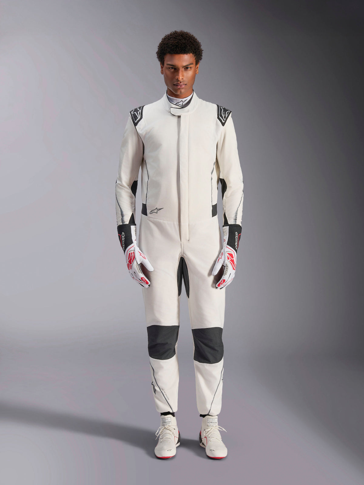 Fato Alpinestars Hypertech V3, fato de automobilismo profissional, branco, preto e prateado, usado por modelo com luvas vermelhas e brancas e sapatos de corrida brancos a condizer, com painéis de contraste pretos e logótipos Alpinestars, design de corte atlético ajustado