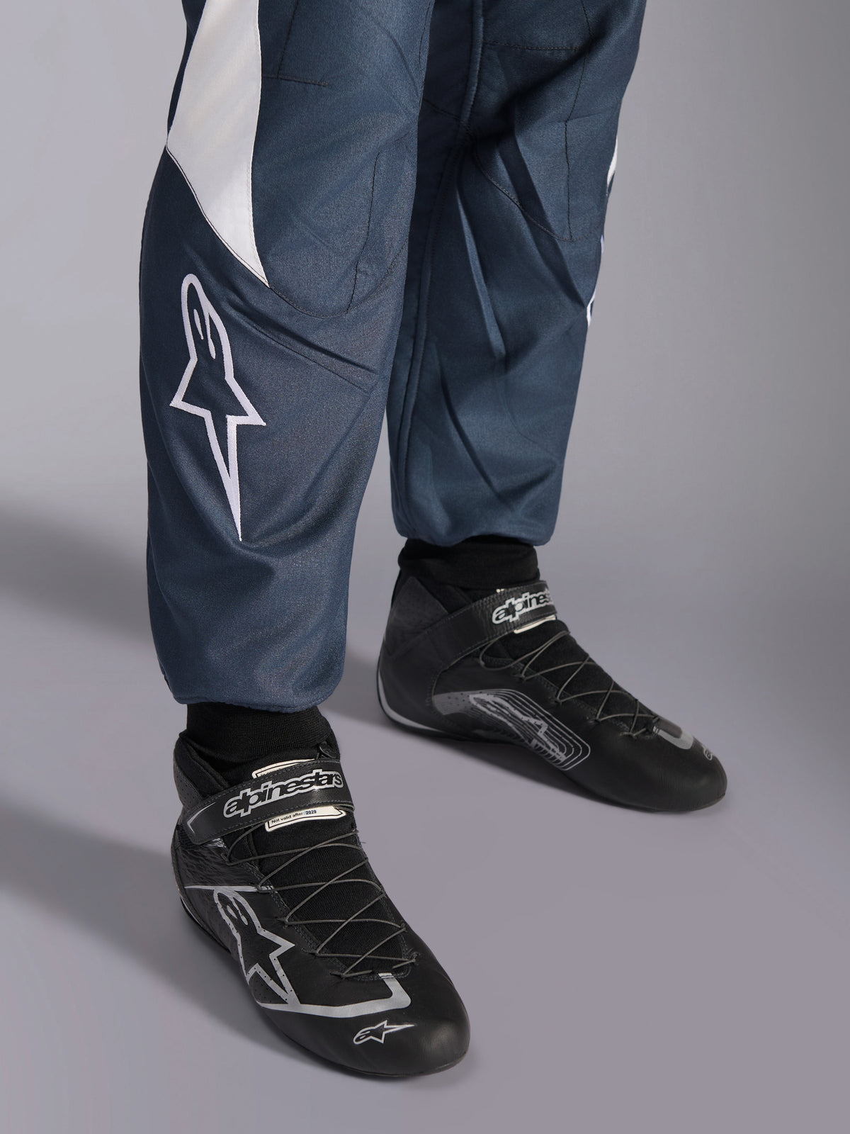 Alpinestars GP Pro Comp V2 Suit, FIA auto racing, Asphalt and Cyan, close-up of star logo and black racing shoes.