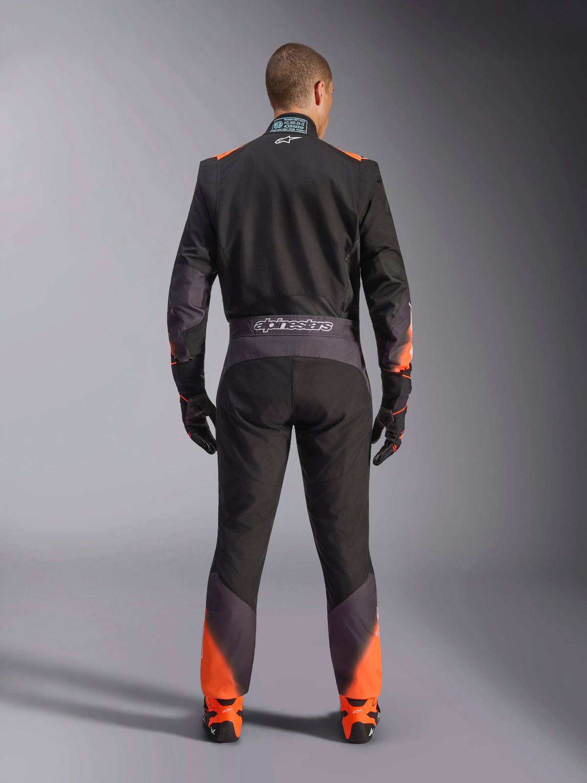 Alpinestars KMX-5 V3 Suit, men's black and orange fluo one-piece karting suit, FIA certified, rear view showing branding.