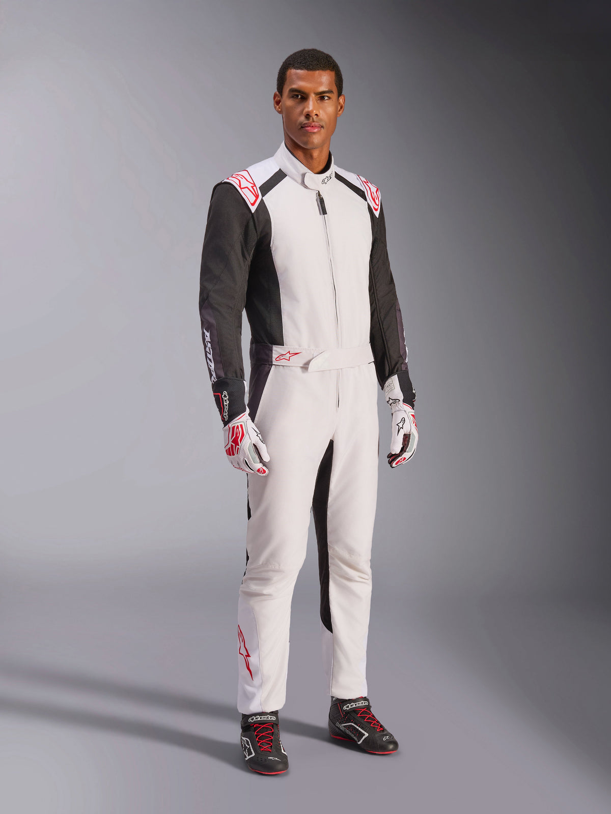 Macacão Alpinestars KMX-5 V3, Branco, Preto e Vermelho Vivo, fato de karting de uma peça usado com luvas brancas e vermelhas a condizer e sapatilhas de corrida pretas, com mangas pretas e pormenores em vermelho vivo, equipamento de desporto motorizado profissional para karting de competição