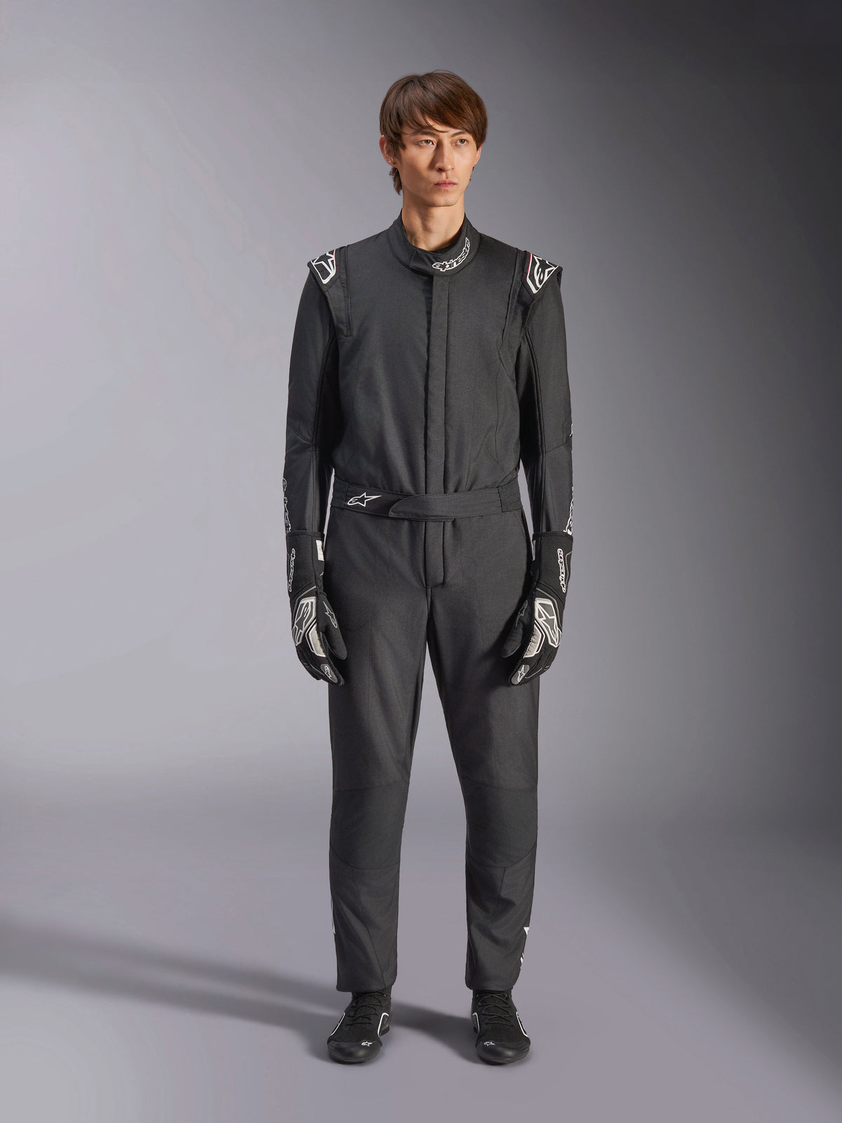 Alpinestars GP Tech V4 Suit, Black and White, professional one-piece auto racing suit, worn with matching black and white gloves and racing shoes, featuring white Alpinestars logos on shoulders and collar, sleek athletic fit for motorsport competition