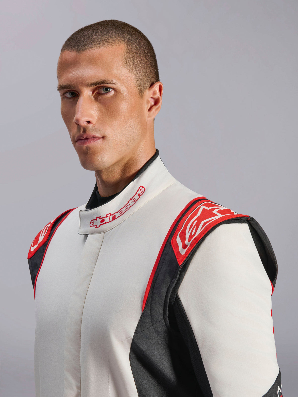 Macacão Alpinestars GP Tech V4, fato de automobilismo, branco, preto e vermelho, vestido por modelo, com painéis vermelhos nos ombros com logótipo Alpinestars, tronco branco com painéis laterais pretos e gola com marca, equipamento profissional de desportos motorizados
