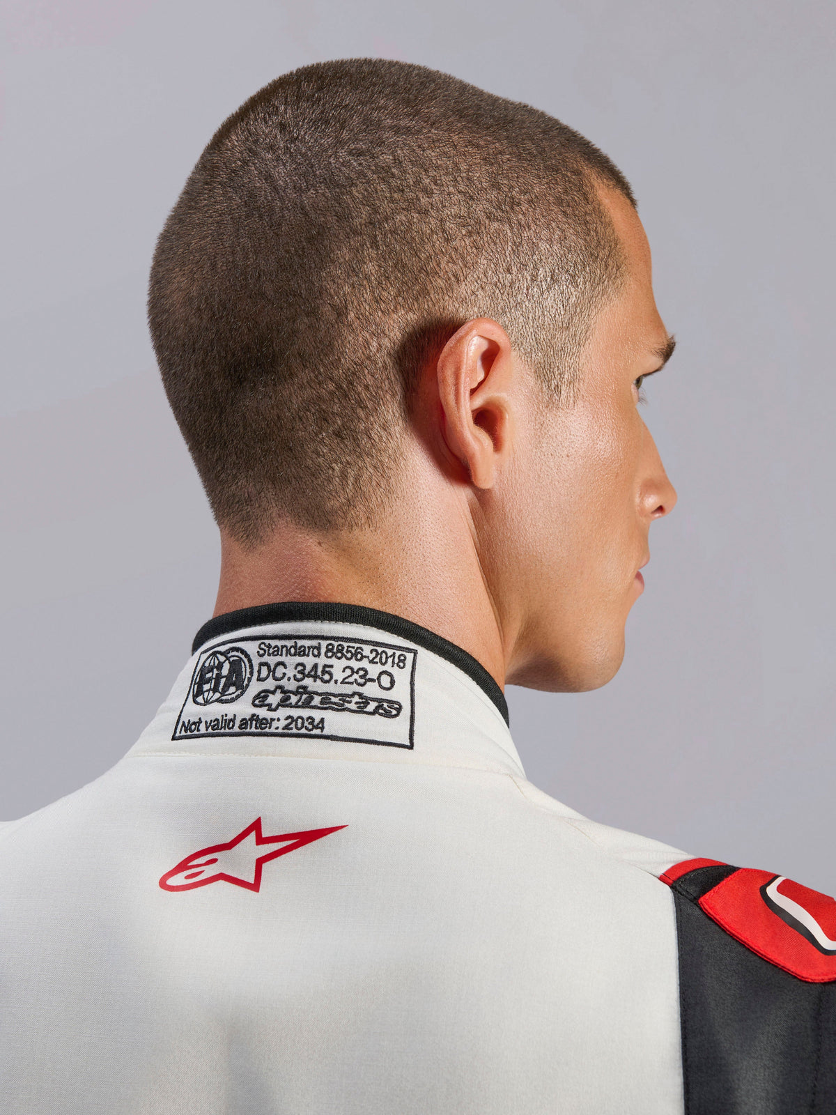 Alpinestars GP Tech V4 Suit, macacão de automobilismo em branco, preto e vermelho, pormenor da gola traseira com a etiqueta de certificação FIA 8856-2018 e o logótipo da estrela em vermelho, equipamento de segurança profissional para automobilismo