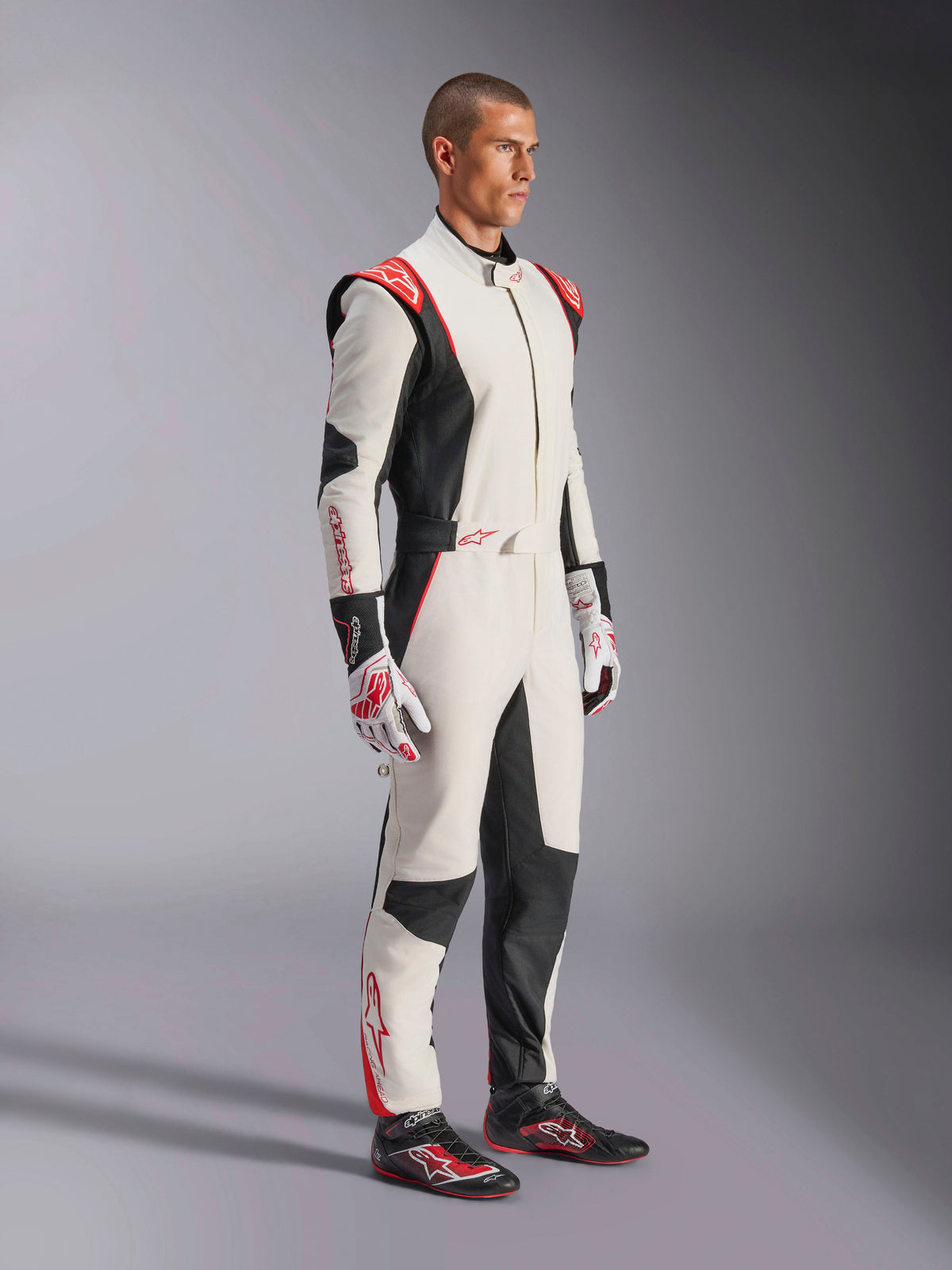 Piloto de corridas masculino a usar o Macacão Alpinestars GP Tech V4, em branco, preto e vermelho, fato de automobilismo de uma peça inteira, luvas e sapatos de corrida a combinar, equipamento profissional de desporto motorizado com logótipos Alpinestars e design ergonómico