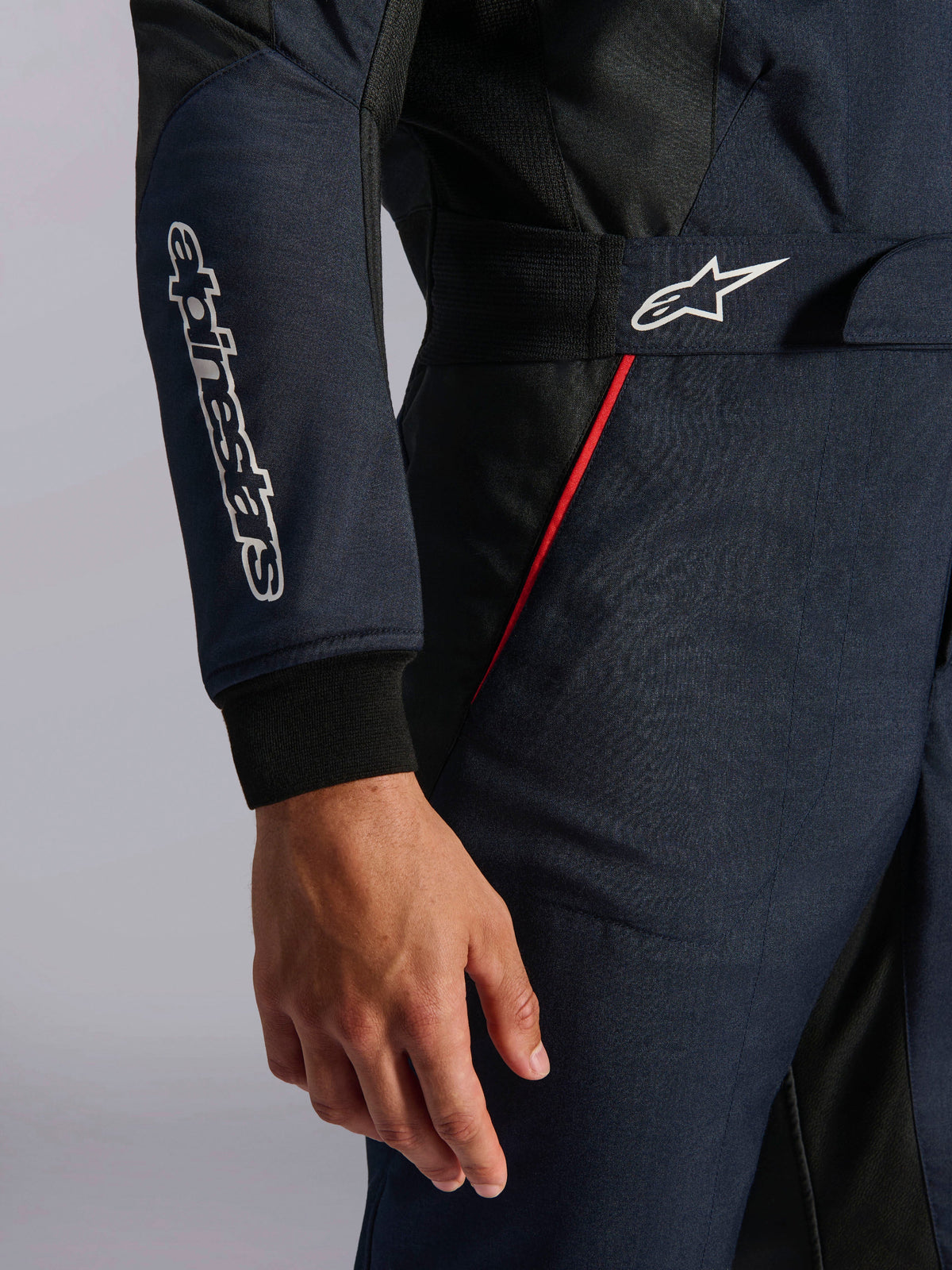 Alpinestars GP Tech V4 Suit in Blue Navy Black Red, detail shot of the waist and sleeve featuring white Alpinestars logos, red accent piping, and textured twill fabric.