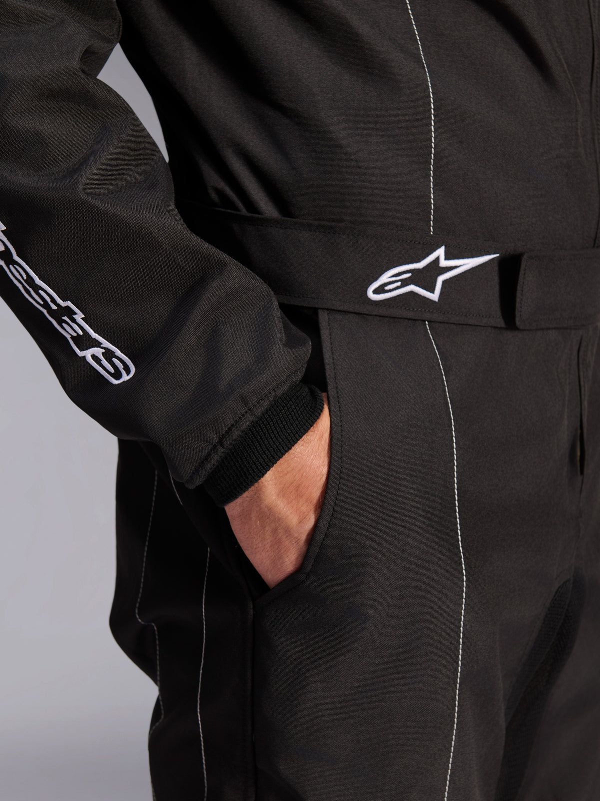 Alpinestars KMX-9 V3 Suit, Black and White, close-up view of adjustable waist belt with embroidered logo, side pocket, white contrast stitching on black fabric, technical karting suit detail