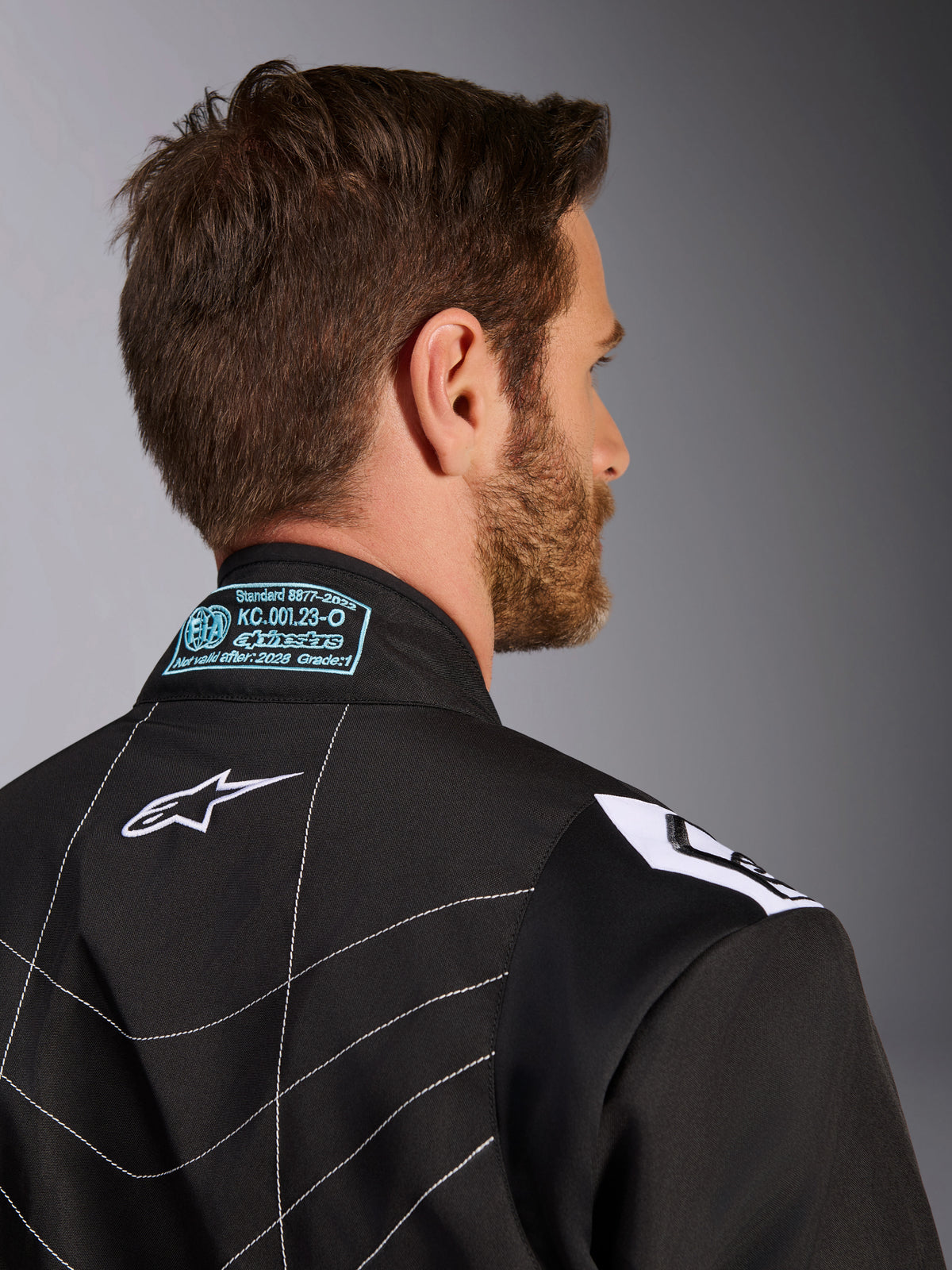 Alpinestars KMX-9 V3 Suit, Black and White, close-up of the back collar and shoulder area, featuring light blue embroidered FIA homologation details, white star logo, and white contrast stitching.
