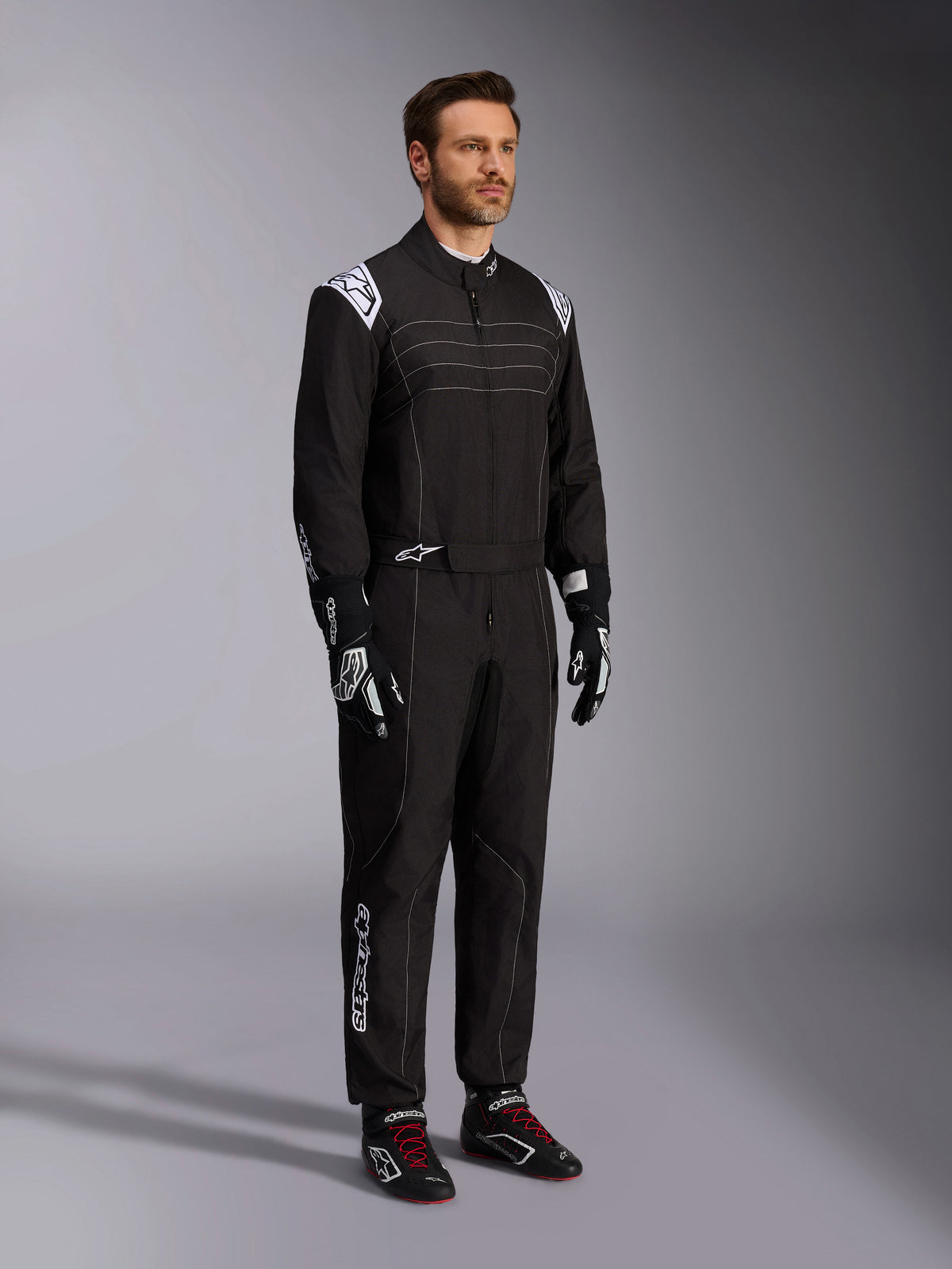 Alpinestars KMX-9 V3 Karting Suit, Black and White, male model wearing full racing suit with white Alpinestars logo on epaulettes, paired with black and white racing gloves and black karting shoes with red laces, studio shot showing the front and side profile