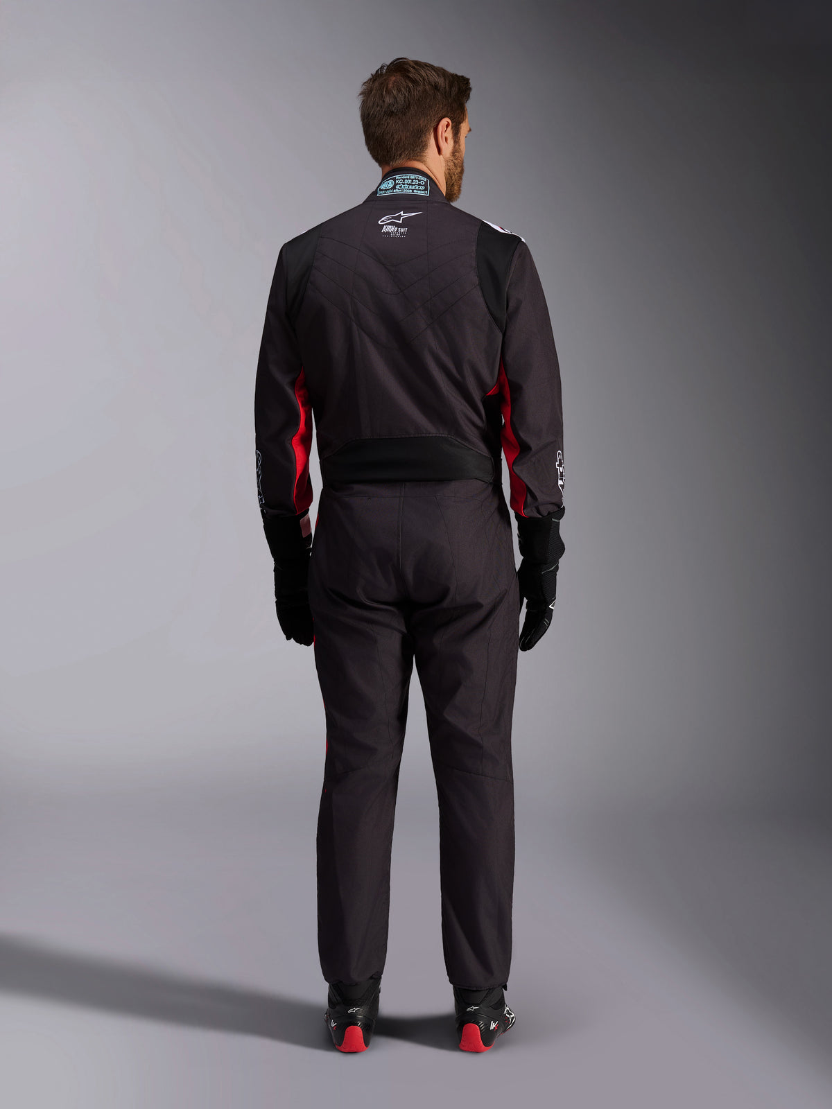 Alpinestars KMX-9 V3 Graphic 3 Suit, Karting Suit, Black and Red, rear view featuring the lumbar stretch panel and FIA certification tag on the collar, styled with black racing gloves and red-accented boots