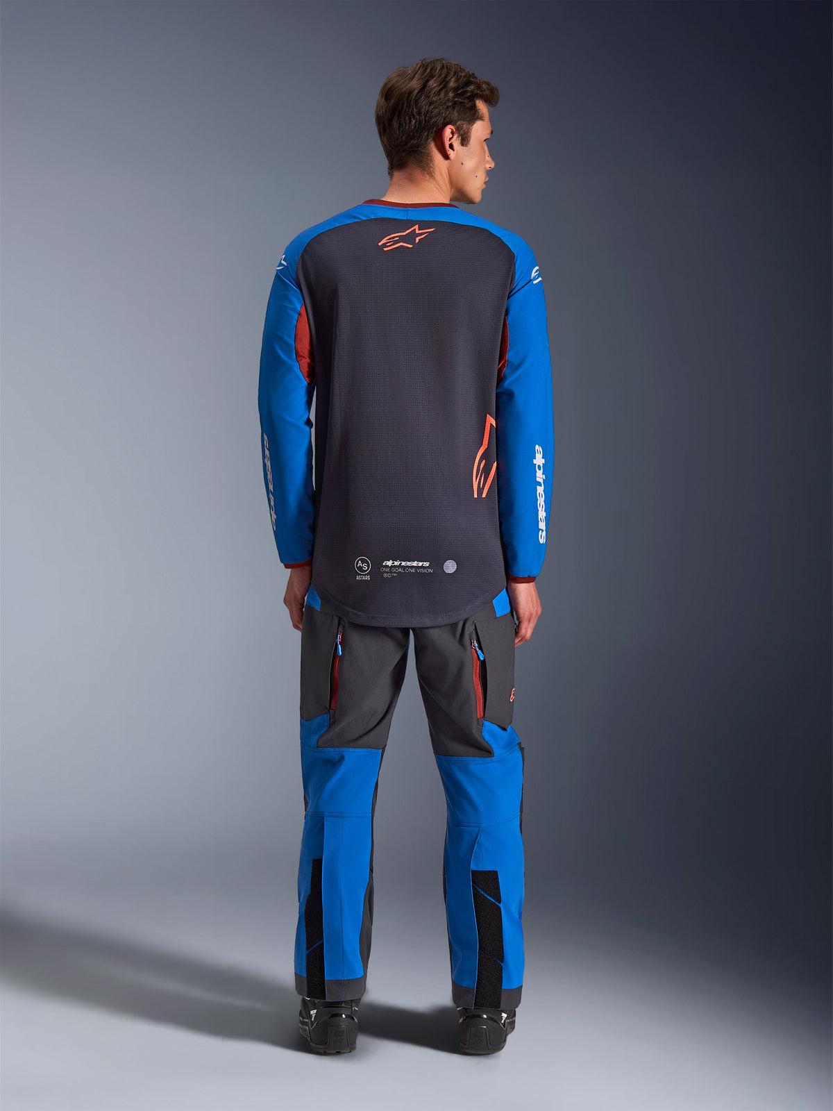 Alpinestars Maxdura Dual Jersey in Deep Gray and Royal Blue, back view showing full mesh torso and orange star logo, royal blue sleeves with white branding, worn with matching gray and blue adventure pants, high-performance gear for dual-sport riding