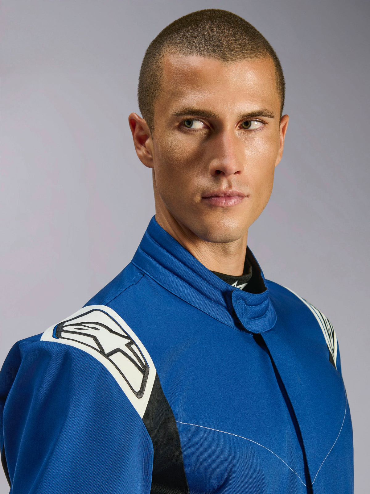 Alpinestars Kart Indoor V2 Suit, fato de karting azul, vista de grande plano de modelo masculino, painéis brancos nos ombros com logótipo de estrela preto, gola ergonómica, sarja de camada única durável para corridas recreativas