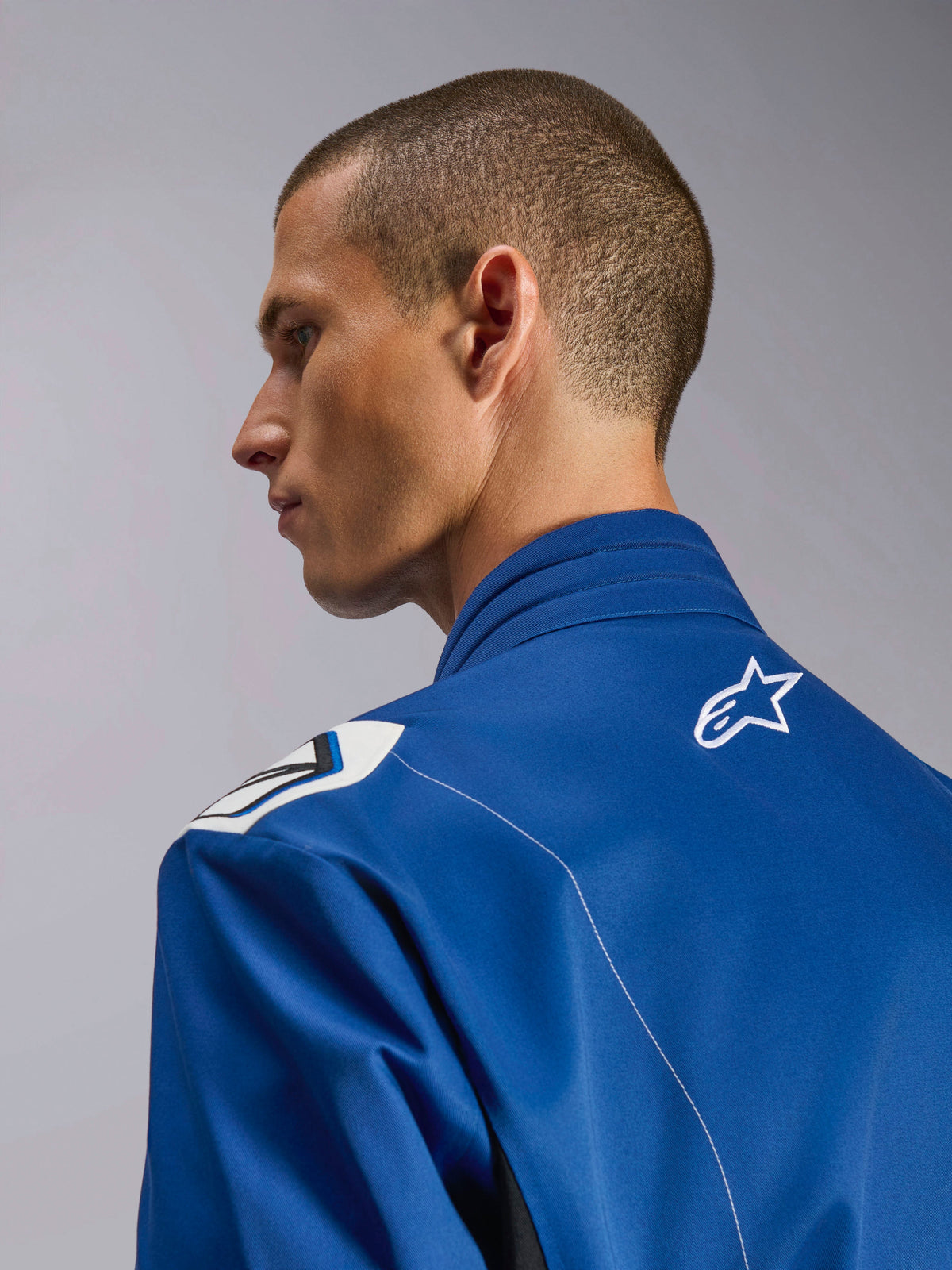 Fato Alpinestars Kart Indoor V2, fato de karting azul, perfil lateral em grande plano da gola ergonómica e parte superior das costas com logótipo de estrela branco, com design de ombros inspirado na Fórmula 1 e construção durável em sarja de poli-algodão
