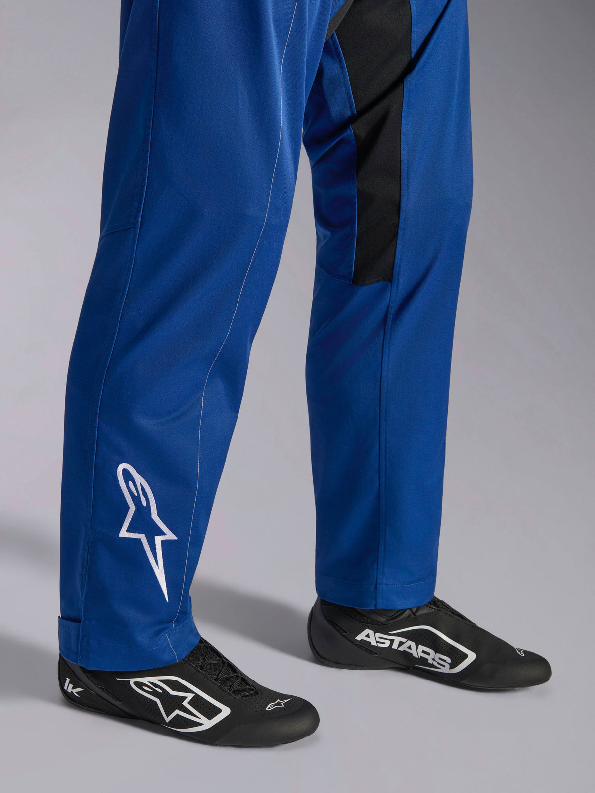 Fato Alpinestars Kart Indoor V2, azul, grande plano da parte inferior das pernas e pés mostrando o logótipo de estrela branca no tornozelo, bainhas das pernas ajustáveis e sapatos de corrida pretos, vestuário de karting durável para uso recreativo em pista
