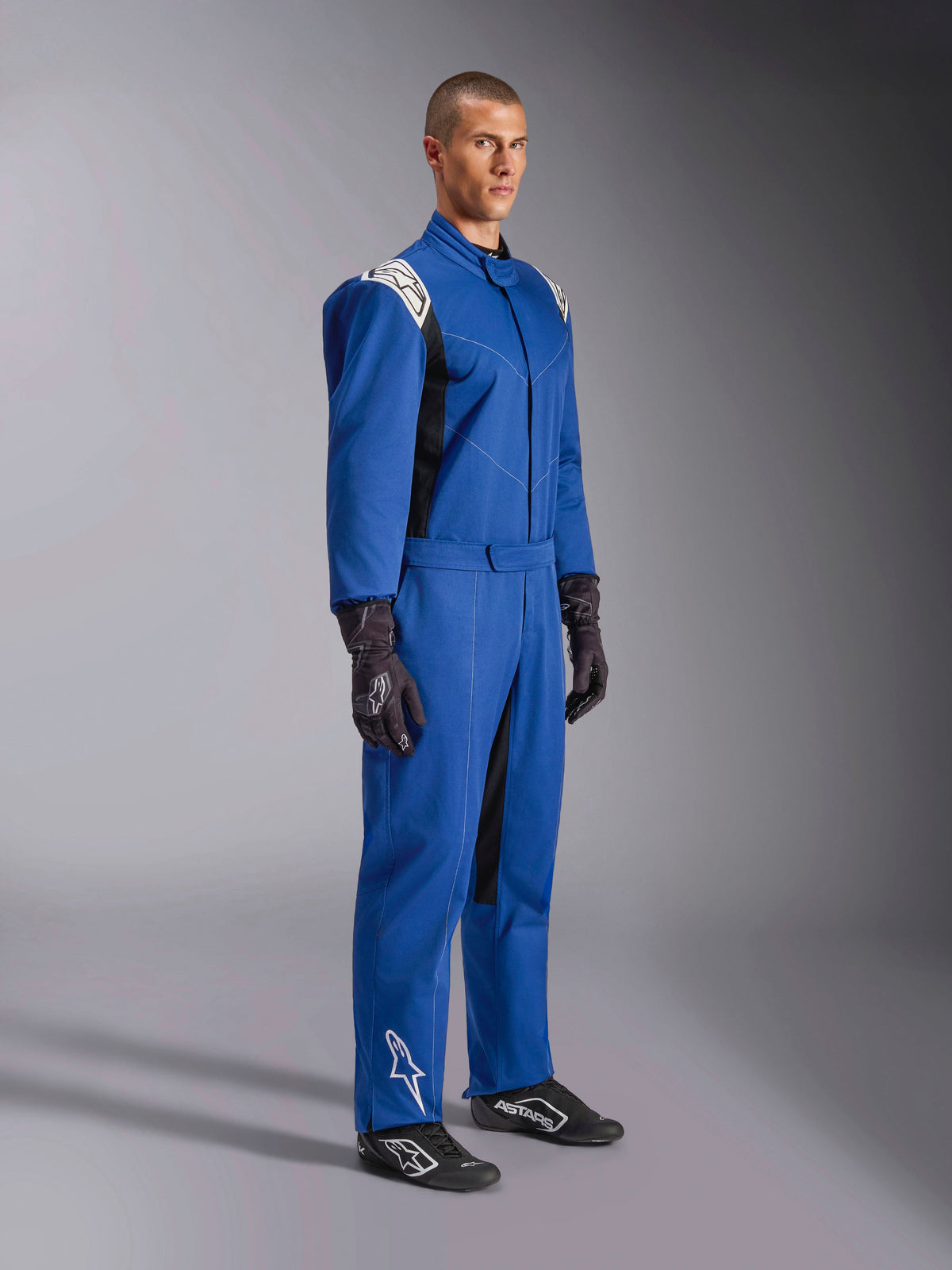 Fato Alpinestars Kart Indoor V2, fato de karting azul, macacão de corrida de peça única com painéis brancos nos ombros e logótipos, cinto ajustável na cintura, logótipo branco na parte inferior da perna, usado por modelo com luvas e sapatos de corrida pretos, vestuário de desportos motorizados para karting indoor