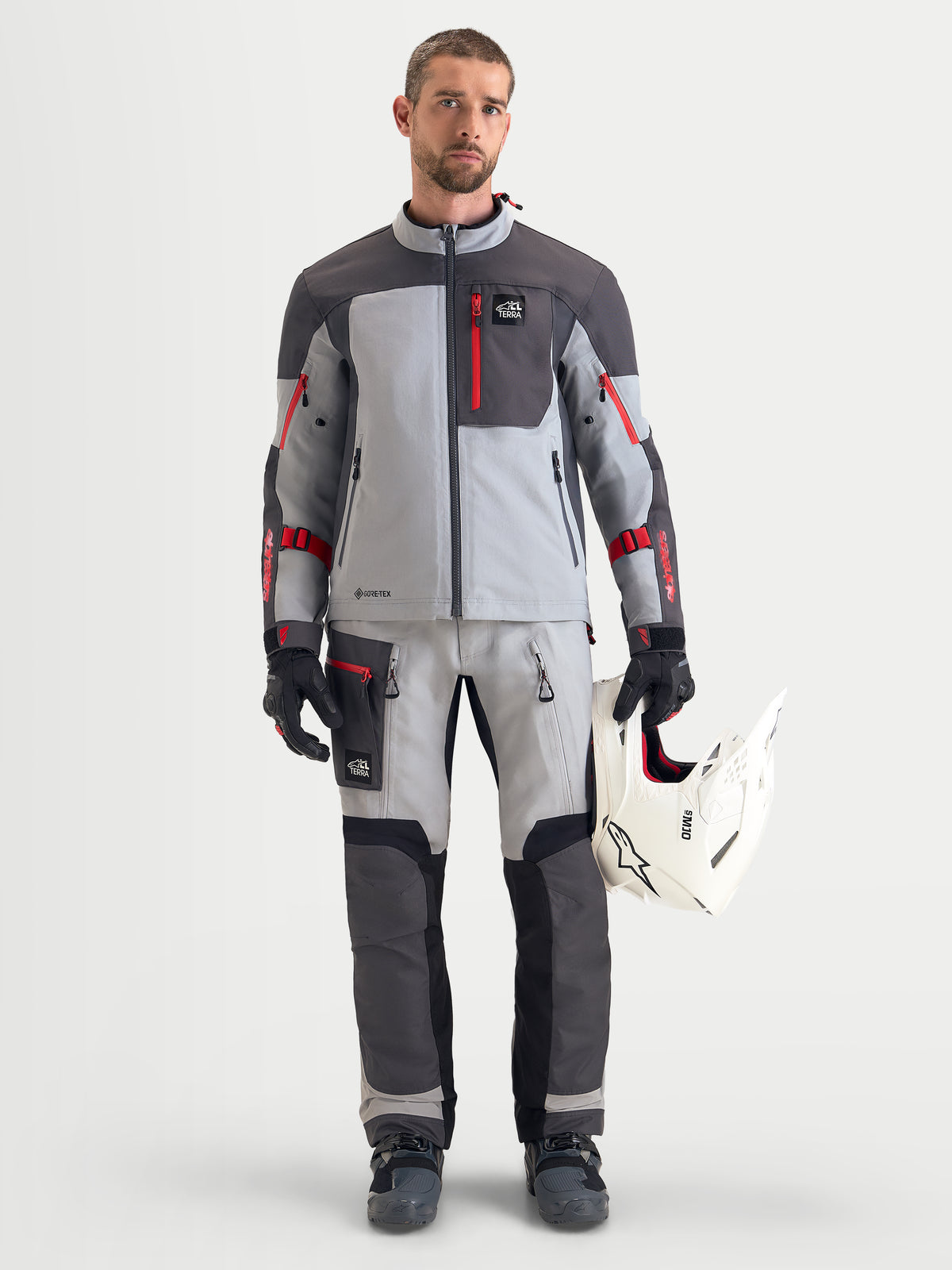 Alpinestars Arenis Gore-Tex, casaco de moto para aventura para homem em cinzento-médio, cinzento-escuro e preto, vestido por um modelo que segura um capacete branco
