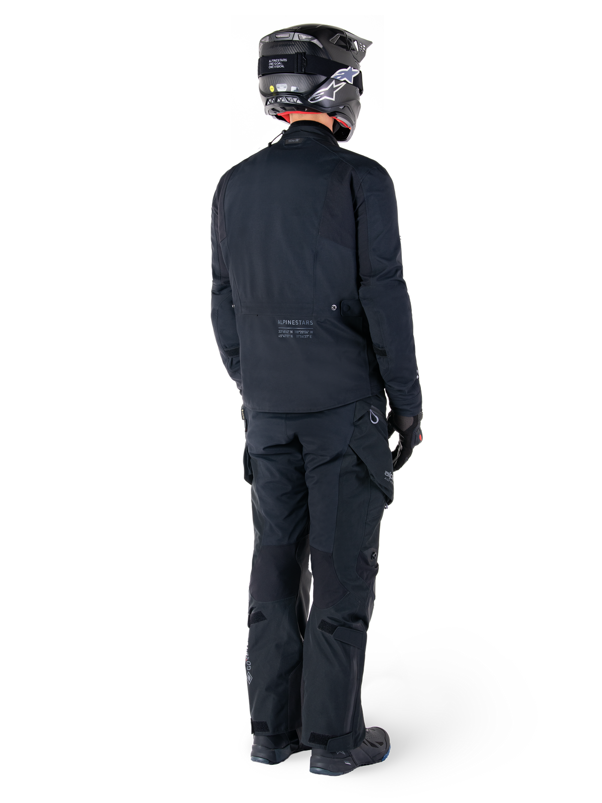 Vista traseira de um motociclista com o casaco Alpinestars St-7 Prime GORE-TEX em preto, combinado com calças de turismo pretas a condizer, capacete de motociclismo preto com logótipo branco e botas de condução pretas; equipamento de aventura protetor completo para turismo e deslocações urbanas.