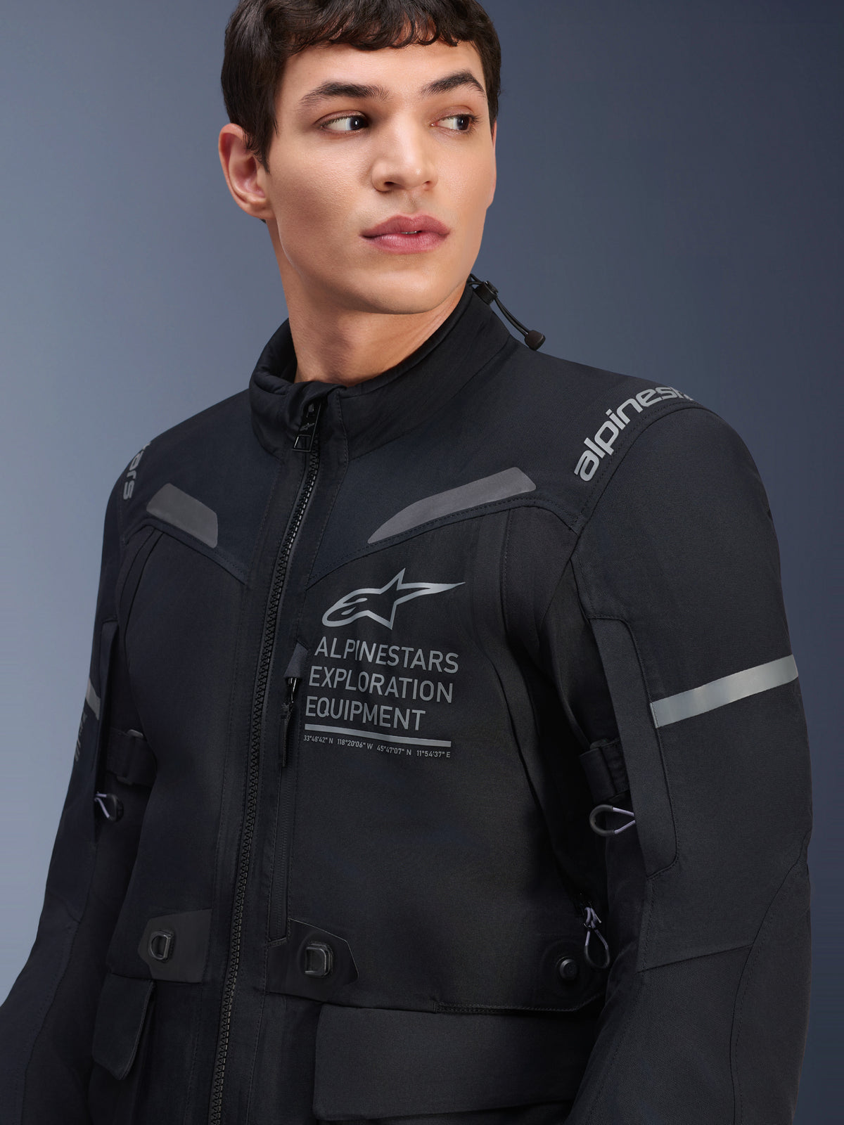 Casaco Alpinestars ST-7 2L GORE-TEX, casaco de motociclismo, preto e cinzento escuro, vestido por um modelo masculino, com a marca Alpinestars Exploration Equipment no peito, detalhes refletores cinzentos e construção têxtil preparada para aventura