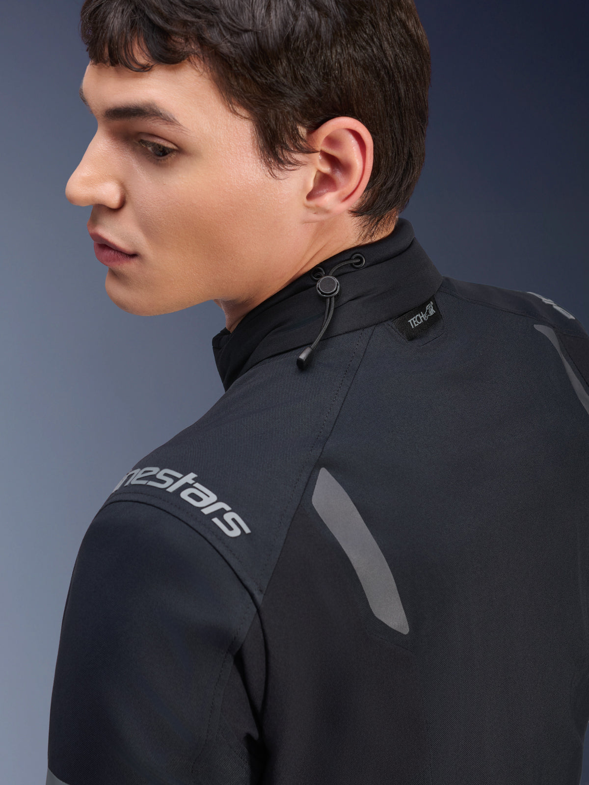 Casaco Alpinestars ST-7 2L GORE-TEX, casaco de motociclismo preto e cinzento escuro, vista em pormenor da gola com ajuste por cordão elástico e etiqueta Tech-Air, detalhes refletores cinzentos e logótipo da marca no ombro