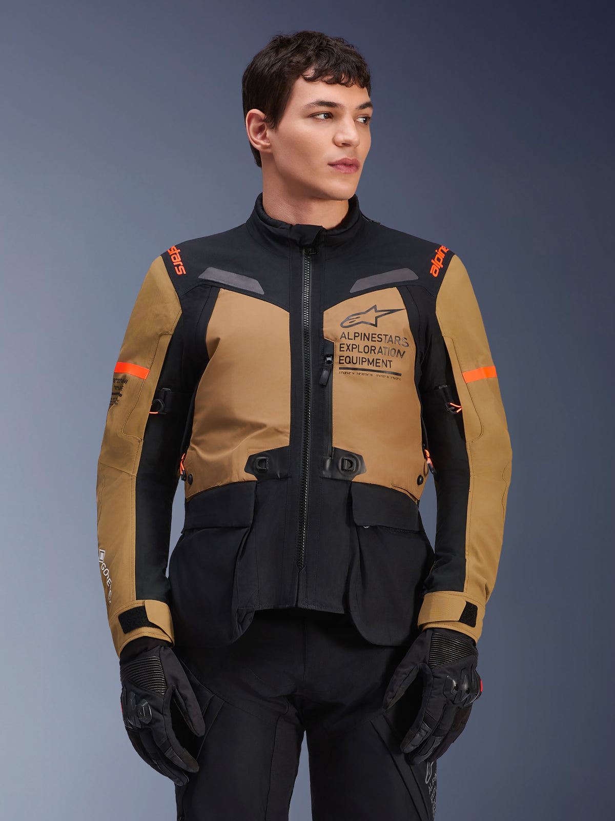 Alpinestars ST-7 2L GORE-TEX Jacket, casaco de motociclismo para turismo e aventura, castanho Gobi e preto com detalhes laranja, vestido por um modelo masculino, com marca Exploration Equipment e tecnologia GORE-TEX, equipamento impermeável e durável