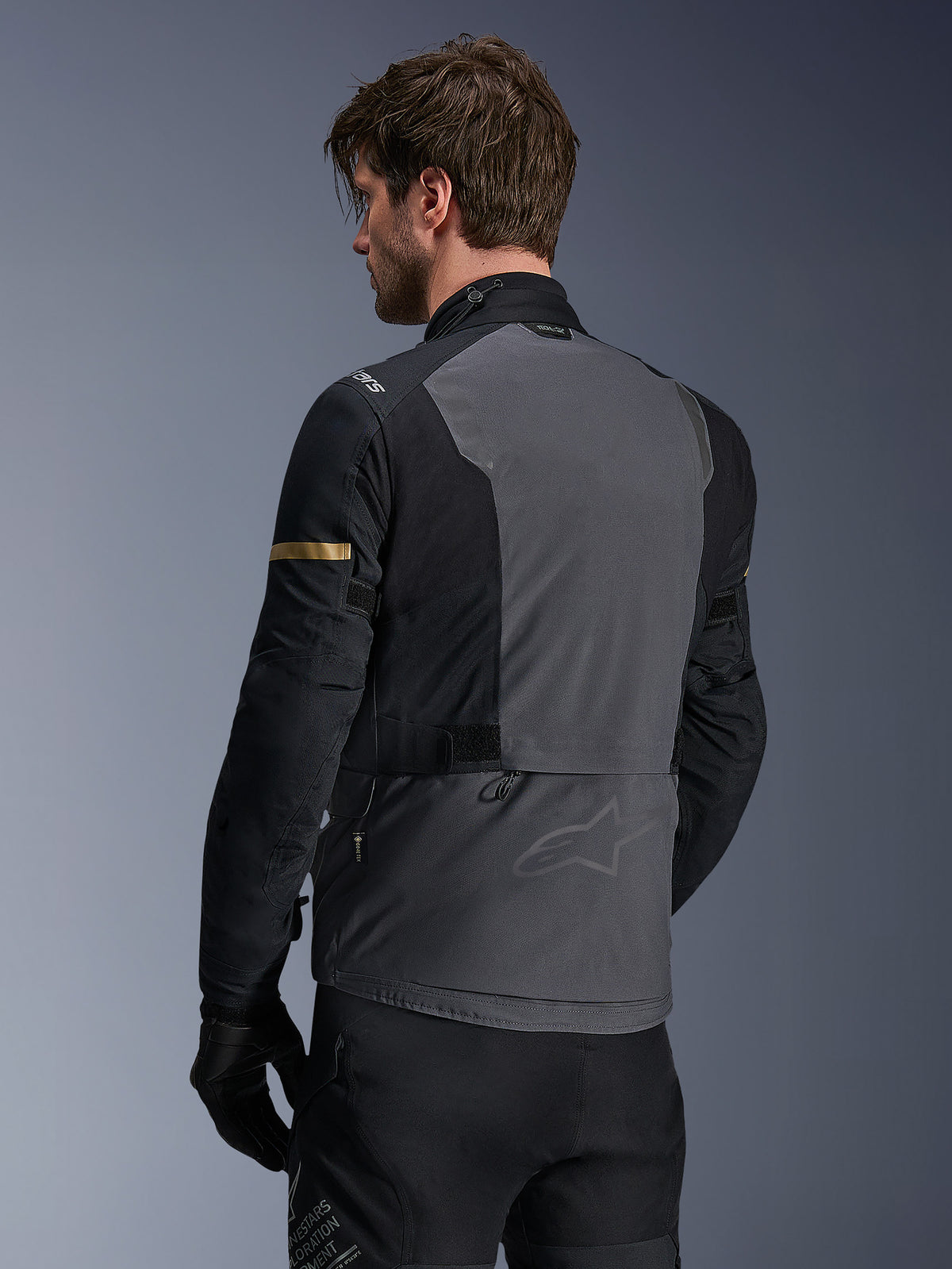 Casaco Alpinestars ST-7 2L GORE-TEX, casaco de motociclismo, cinzento escuro, preto e cáqui escuro, vista traseira apresentando um grande painel traseiro cinzento com marca subtil, mangas pretas com detalhes em cáqui de tom dourado, design têxtil impermeável pronto para a aventura