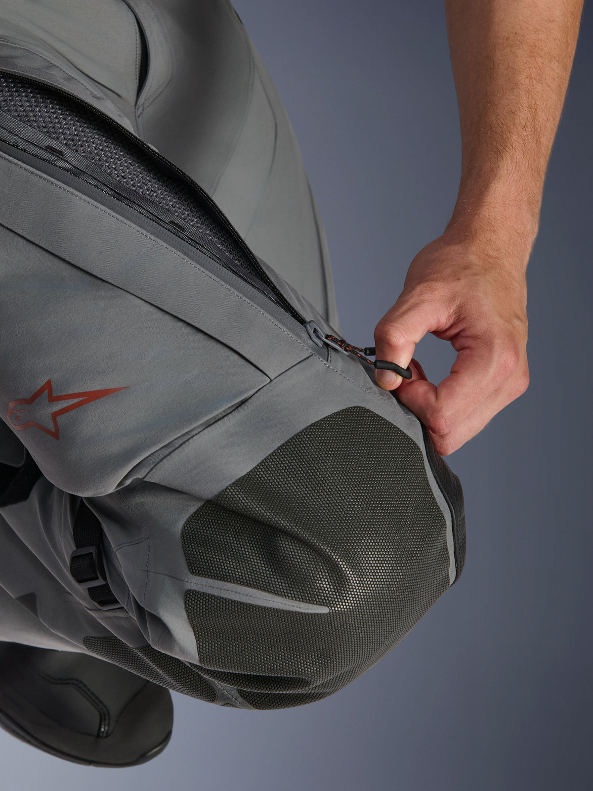 Alpinestars Nazca 3L GORE-TEX PRO Pants, Adventure Motorcycle Pants, Dark Gray and Black, close-up of a hand opening the zippered thigh ventilation intake, featuring textured Superfabric knee reinforcements and a red Alpinestars star logo, technical textile construction for all-weather protection