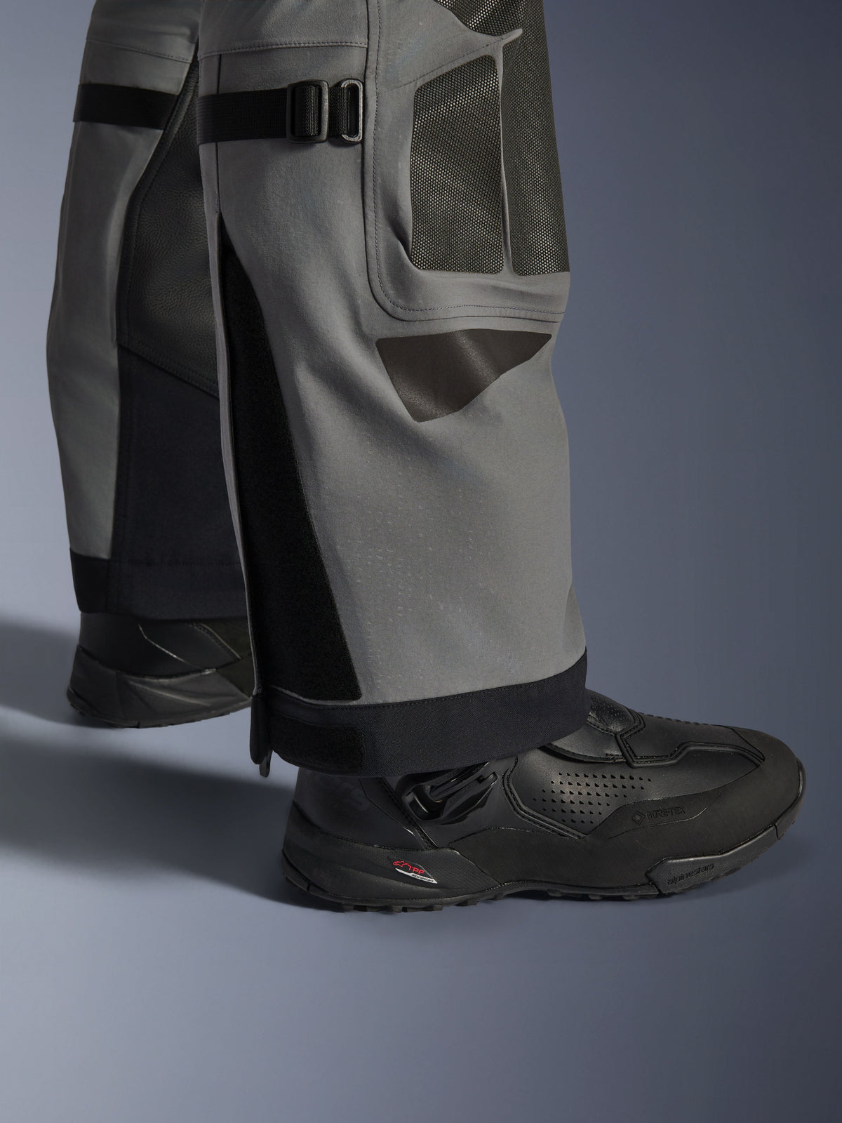 Alpinestars Nazca 3L GORE-TEX PRO Pants, Adventure Motorcycle Pants, Dark Gray and Black, close-up of lower legs featuring calf volume adjusters and Superfabric reinforcements, worn with black Alpinestars boots, durable textile for extreme adventure riding