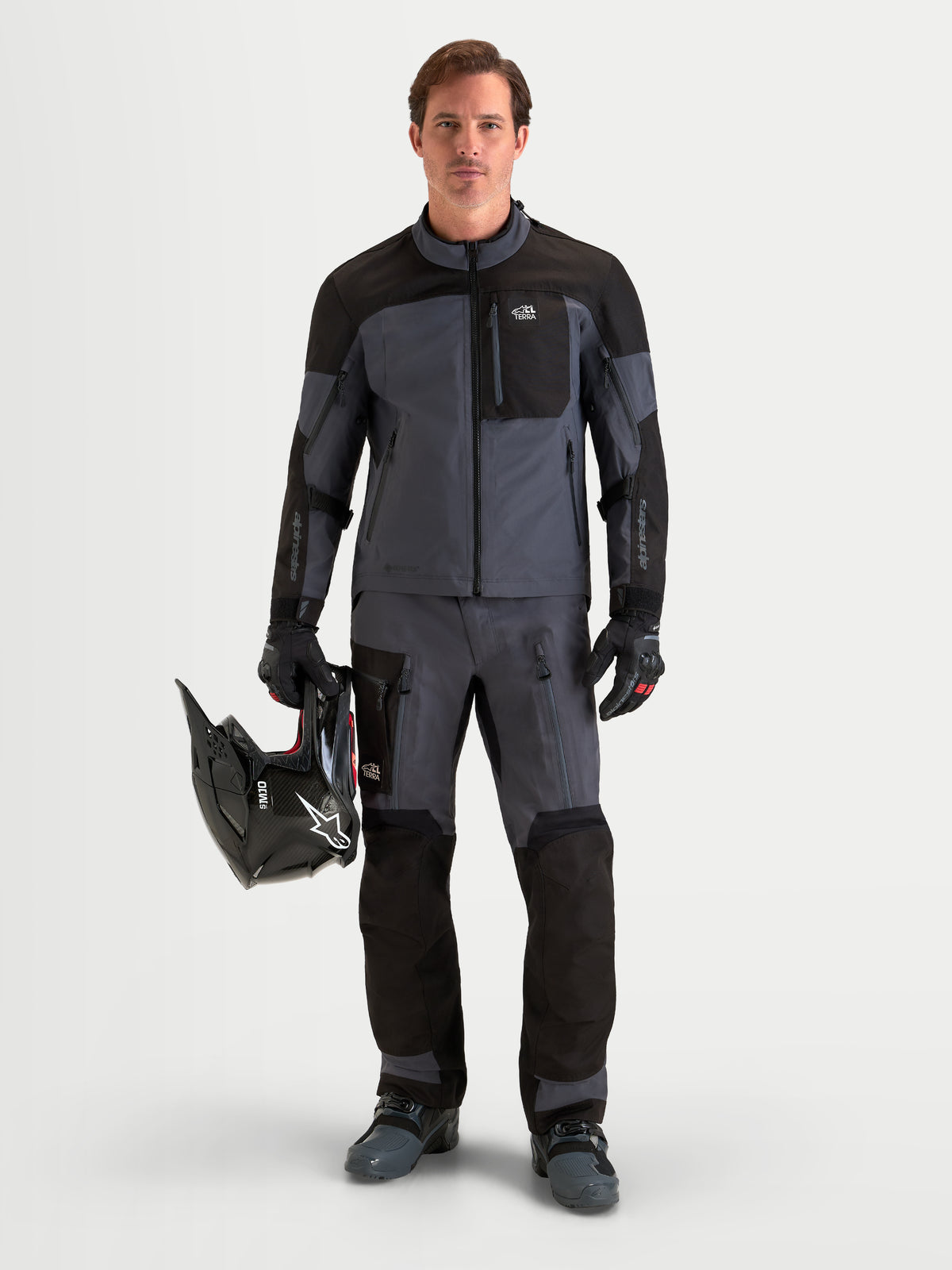 Alpinestars Arenis Gore-Tex calças de moto adventure para homem, em preto e cinzento escuro, vista frontal num modelo a usar equipamento a condizer, capacete e vestuário impermeável