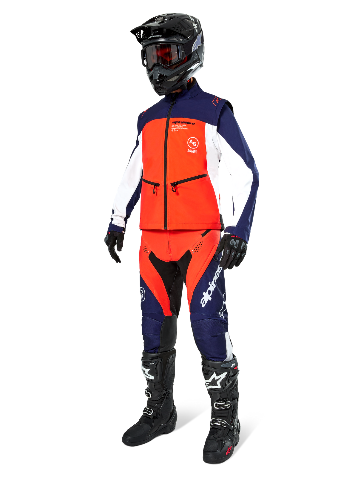 Piloto de motocross com o Casaco Alpinestars Lite-Dura Softshell em azul-marinho, laranja vibrante e branco, calças de todo-o-terreno a condizer, capacete preto com óculos e botas de corrida pretas, conjunto de equipamento de enduro coordenado