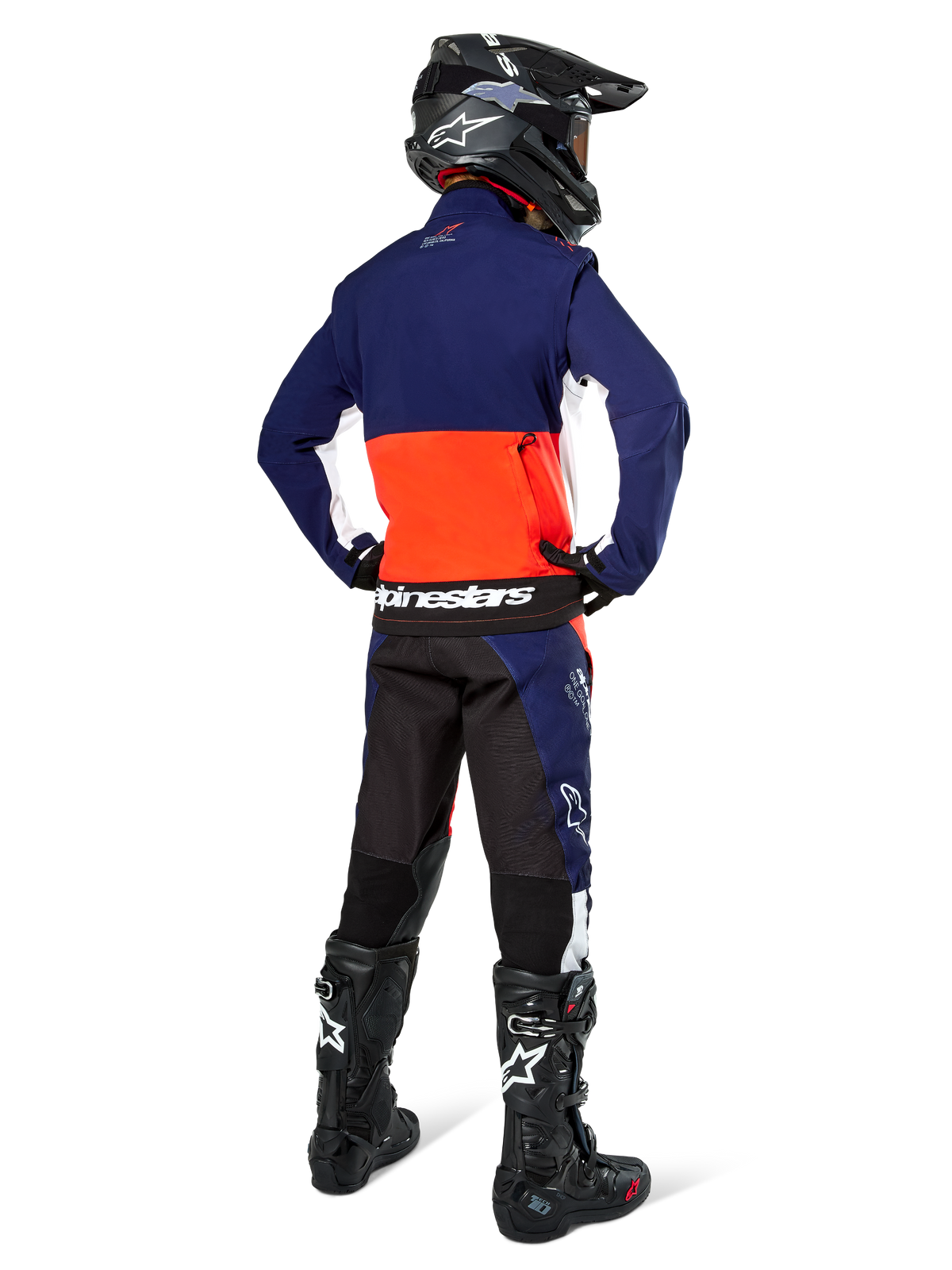 Piloto de motocross visto de costas a usar o casaco Alpinestars Lite-Dura Softshell em azul-marinho, laranja vibrante e branco, mostrando o grande bolso de arrumação traseiro. Combinado com calças de enduro a condizer, capacete de motocross preto e botas de off-road pretas.