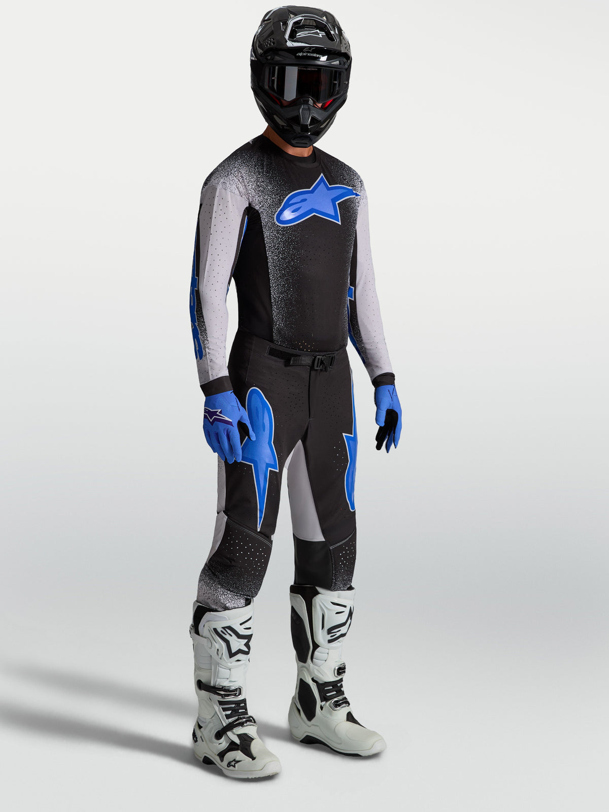 Alpinestars Supertech Hiten AFD, calças de motocross para homem, pretas e azuis, em modelo com camisola e botas brancas.