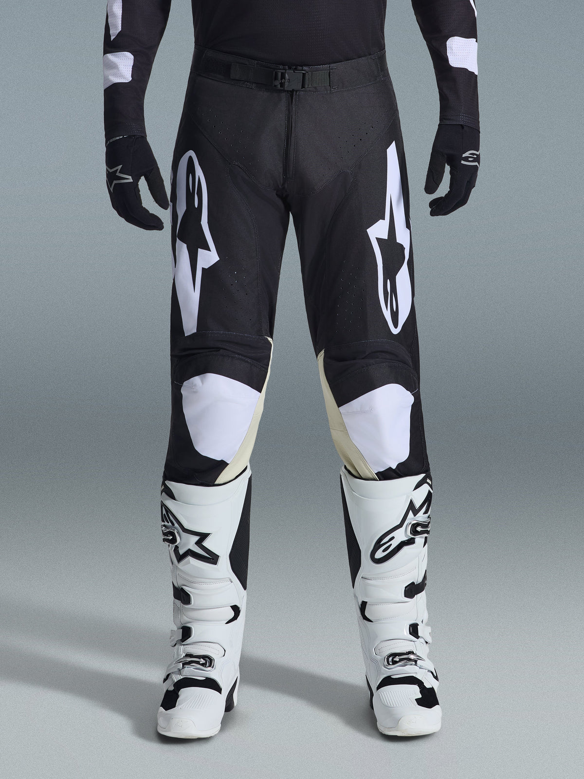 Alpinestars 2026 Racer Air Riway Pants, calças de motocross, pretas e brancas, com logótipos Alpinestars brancos em destaque nas coxas e nos painéis dos joelhos, combinadas com botas de motocross brancas e pretas e luvas pretas, design de ajuste desportivo de corrida para condução off-road