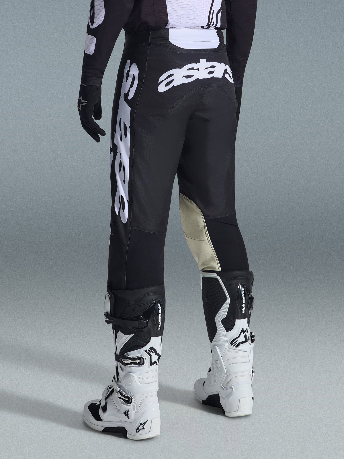 Vista traseira das calças Alpinestars Racer Air Riway 2026 em preto e branco, com logótipo 'astars' proeminente em branco no assento e na perna, painéis interiores dos joelhos em pele creme, usadas com botas e camisola de motocross pretas e brancas a condizer