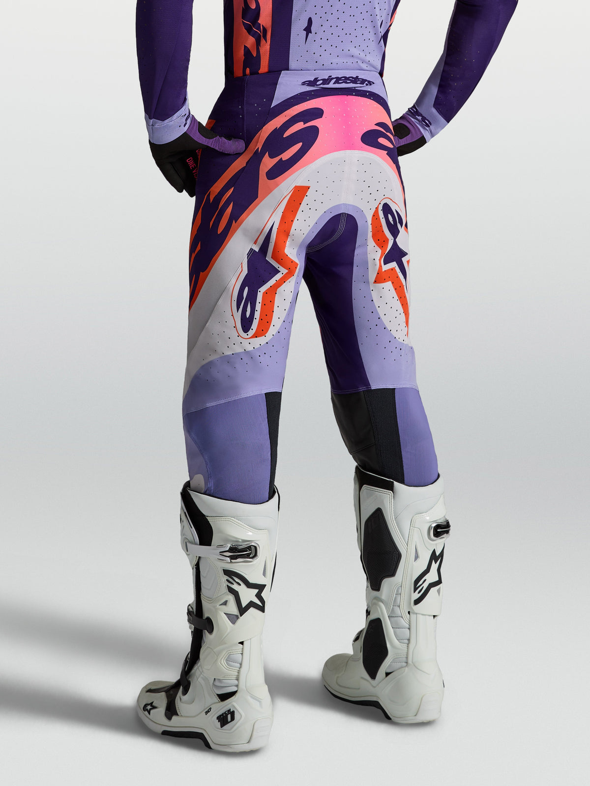 Alpinestars Supertech Dyna, calças de motocross para homem, roxo e violeta com detalhes rosa fluo, vista traseira em modelo, construção em tecido elástico respirável para alto desempenho
