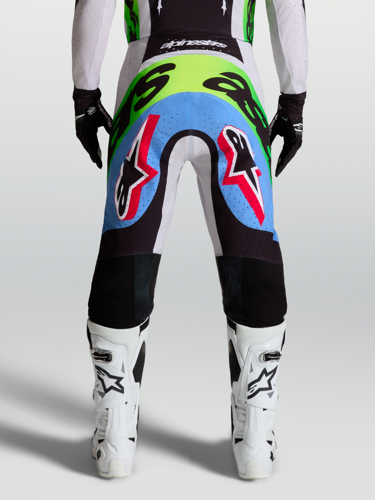 Alpinestars calças Supertech Dyna, calças de motocross para homem, vista traseira lilás e verde fluo com painéis perfurados.