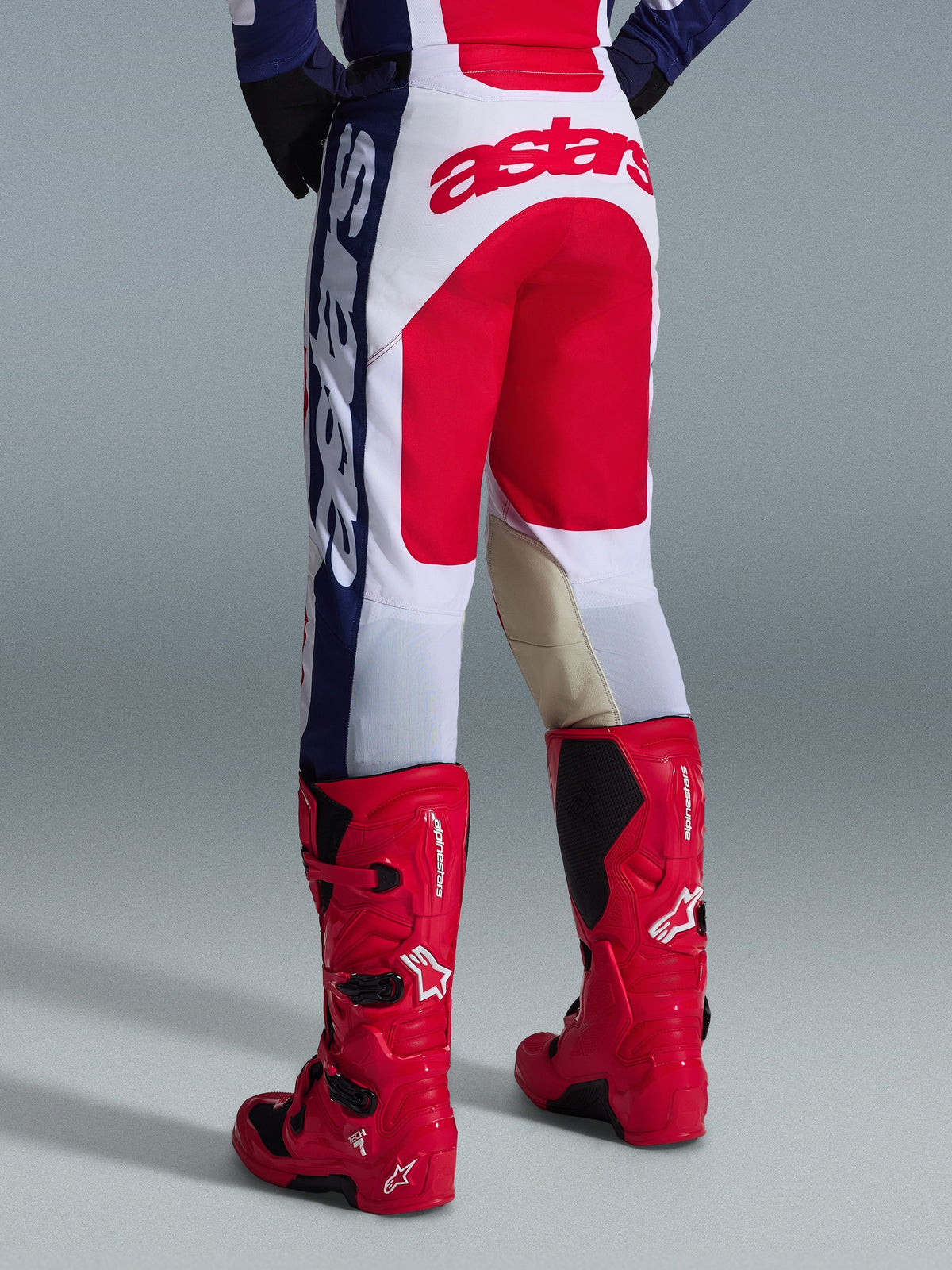 Calças Alpinestars 2026 Racer Riway, calças de motocross, brancas, azuis e vermelhas, vista traseira com grande logótipo Astars vermelho no assento e painéis internos dos joelhos em couro bege, combinadas com botas de motocross Alpinestars vermelhas, equipamento de performance para off-road