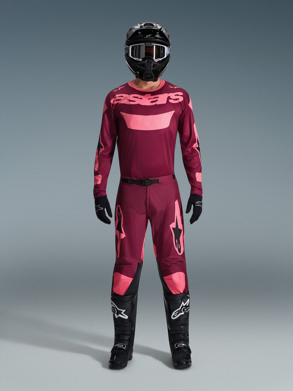Piloto de motocross com equipamento de corrida completo, Camisola Racer Riway 2026 em Dark Red Coral, calças em vermelho escuro com detalhes coral a condizer, capacete preto com detalhes brancos, botas pretas com logótipos brancos e luvas pretas, conjunto coordenado para corridas off-road