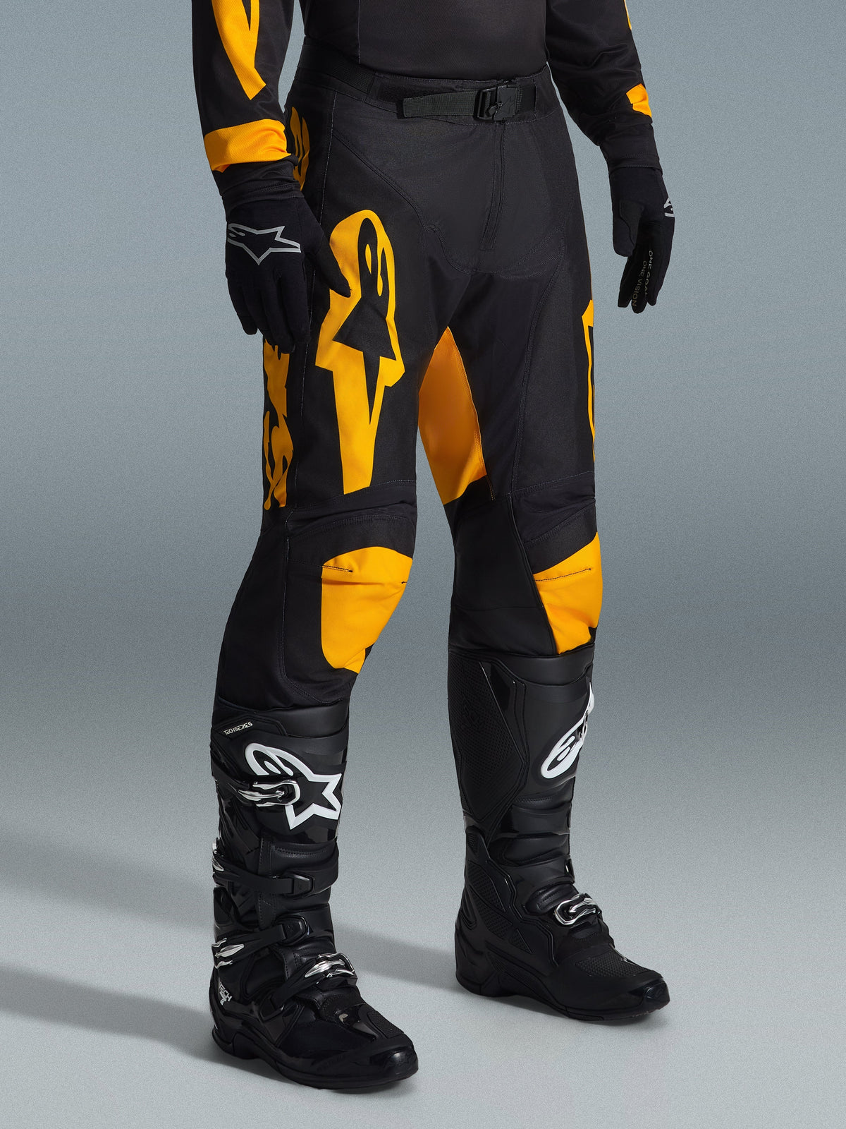 Calças Alpinestars Racer Riway 2026, calças de motocross, amarelas e pretas, usadas com luvas pretas e botas de motocross pretas, com logótipos Alpinestars em amarelo vibrante e detalhes nos joelhos sobre uma base preta, concebidas para corridas todo-o-terreno de alta performance
