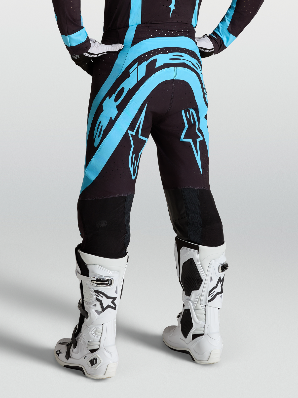 Alpinestars Supertech Vesta, calças de motocross para homem, pretas e azul turquesa, vista traseira, com botas brancas.