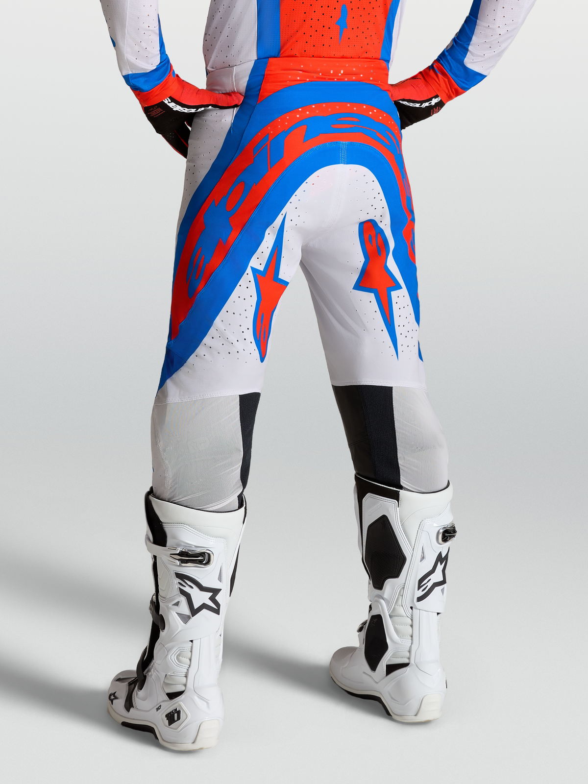 Alpinestars Calças Supertech Vesta, calças de motocross para homem, brancas, vermelhas e azuis, tecido rip-stop perfurado, vista traseira em modelo com botas