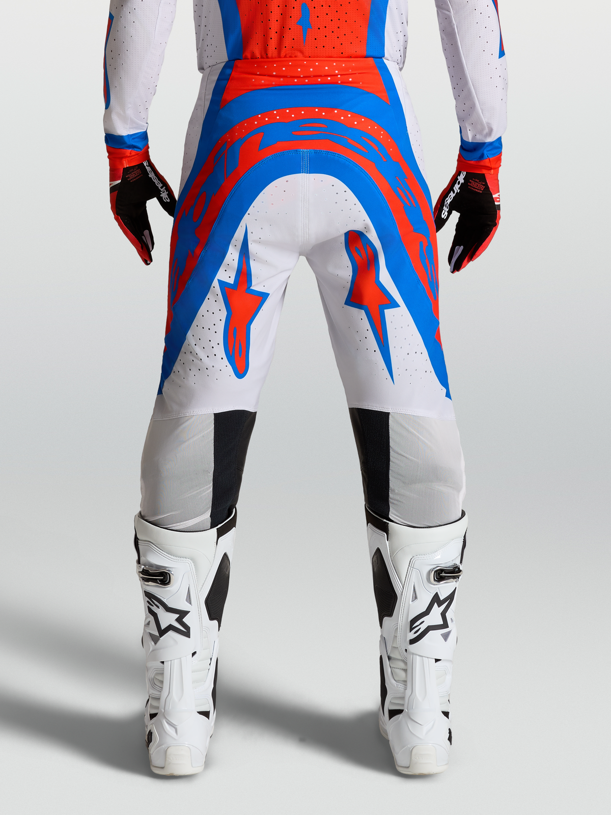 Alpinestars Calças Supertech Vesta, calças de motocross para homem, vermelho-cardeal e azul, vista traseira num modelo, tecido elástico ventilado para desempenho off-road