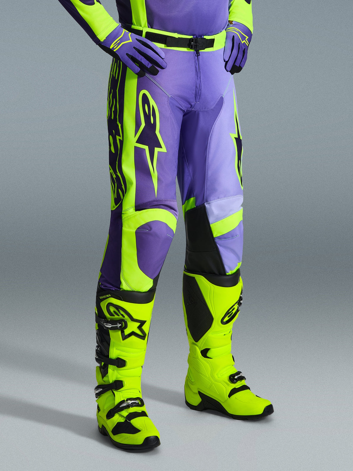 Alpinestars 2026 Racer Portl Pants, calças de motocross em roxo e amarelo néon, usadas por um piloto com botas amarelo néon a condizer e luvas roxas, com a marca Alpinestars em destaque e design ergonómico para performance off-road