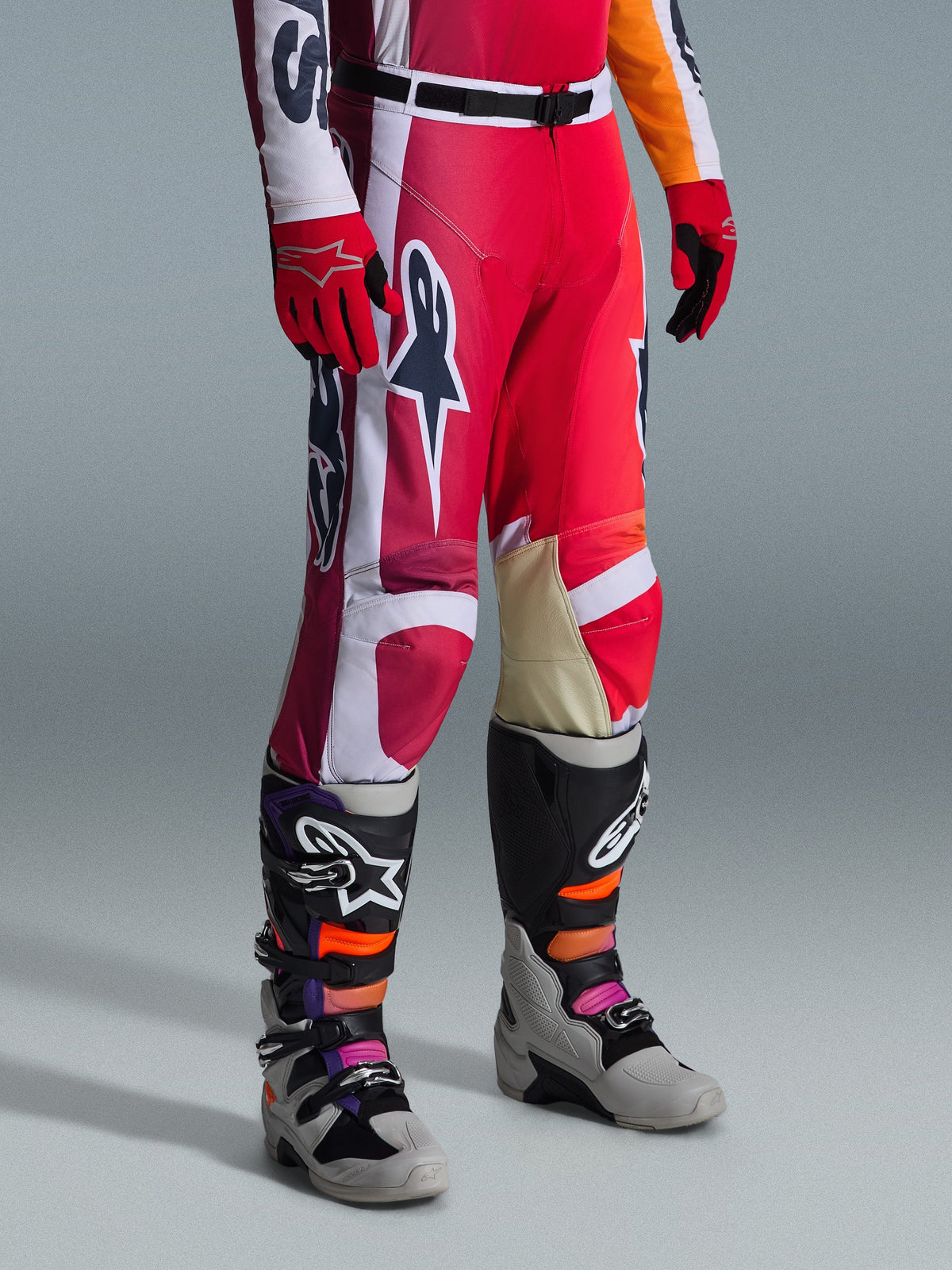Alpinestars 2026 Racer Portl Pants, calças de motocross, vermelhas, cinzento claro e cinzento escuro, usadas com luvas vermelhas a condizer e botas de motocross multicoloridas, com logótipos Alpinestars em destaque e painéis reforçados para corridas de off-road