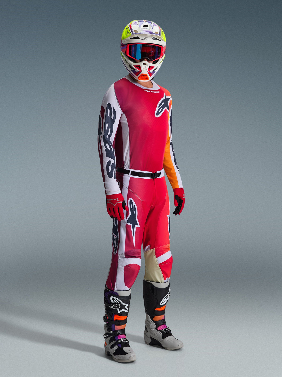 Alpinestars 2026 Racer Portl Pants, calças de motocross, vermelho, cinzento claro e cinzento escuro, usadas como parte de um conjunto de equipamento de corrida completo com camisola a condizer, luvas vermelhas, capacete colorido com óculos azuis e botas cinzentas, construção durável para desempenho em motocross off-road