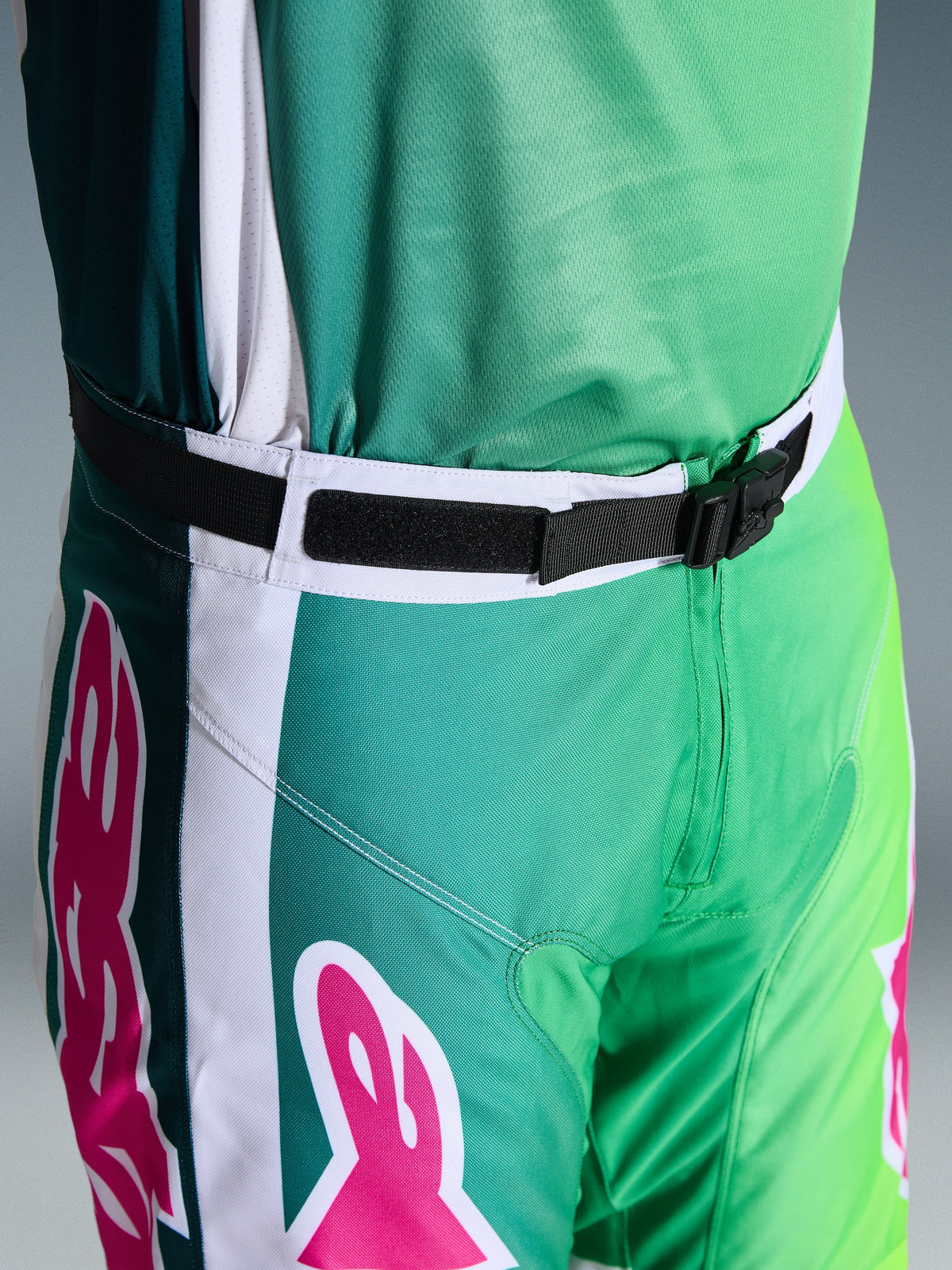 Alpinestars 2026 Racer Portl Pants, calças de motocross, verdes, brancas e pretas com detalhes do logótipo em cor-de-rosa, grande plano da cintura a mostrar a fivela magnética SX2 e o fecho ajustável, equipamento durável para corridas off-road
