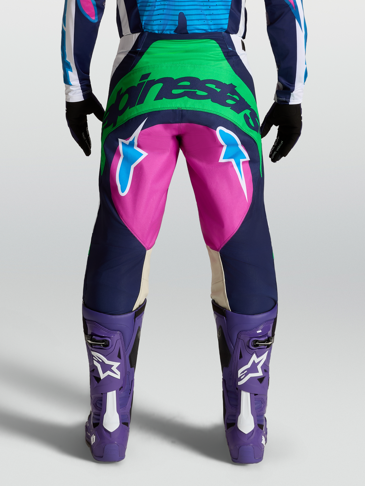 Calças Techstar Maven, calças de motocross azuis e rosa em modelo, vista traseira com logótipo Alpinestars e estrelas.