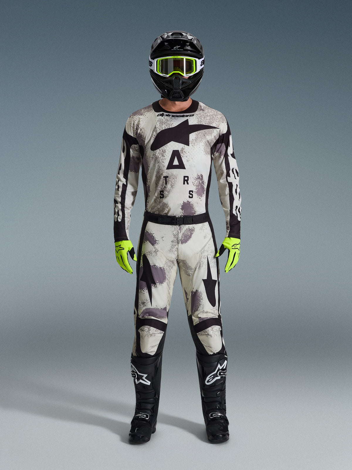 Piloto de motocross a usar a camisola Racer Lahnd 2026 e calças a condizer em Sand Camo, capacete preto com óculos amarelo néon, luvas amarelo néon e botas pretas, conjunto completo de equipamento de corrida off-road da Alpinestars